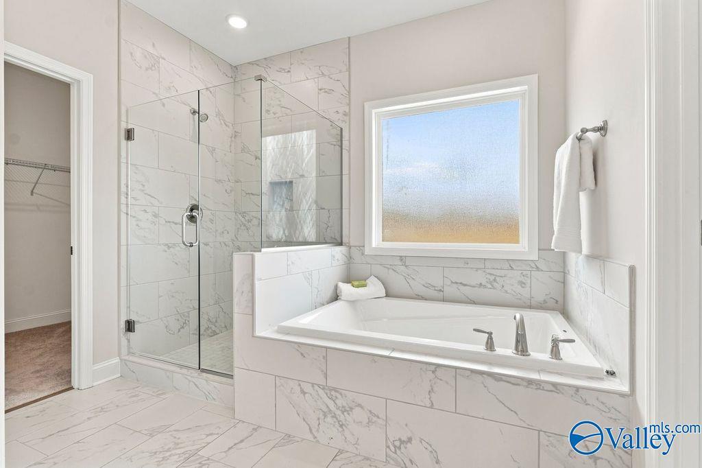 Master bath with soaking tub, glass walk-in shower, and marble tile in The Harrison by Davidson Homes, Hartselle, Alabama