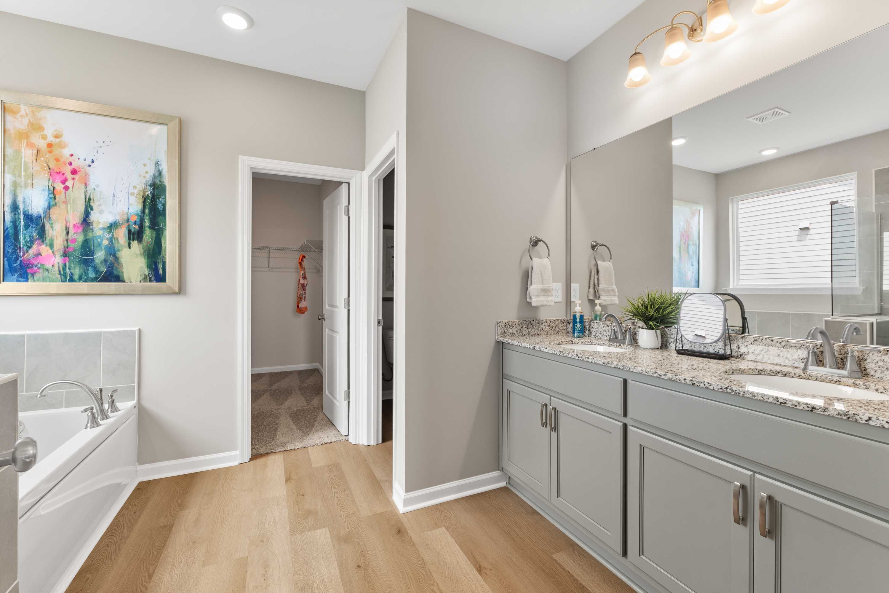 Spacious modern bathroom at The Meadows at Hampton Cove in Owens Cross Roads, Alabama with gray double vanity, soaking tub, and abstract art