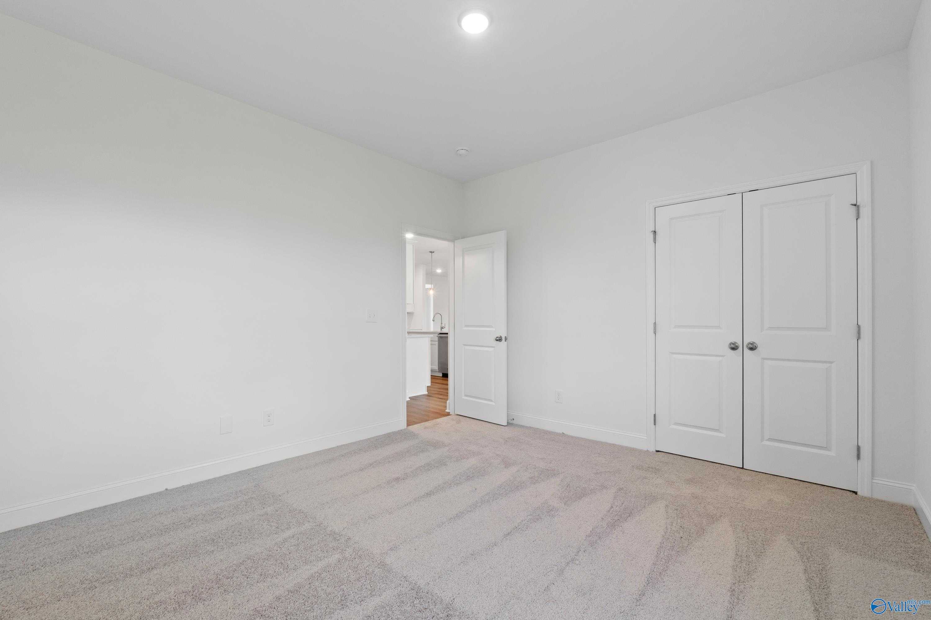 Spacious bedroom with white walls, beige carpet, double closet doors, and en-suite bath access in Davidson Homes The Oxford, Harvest, AL