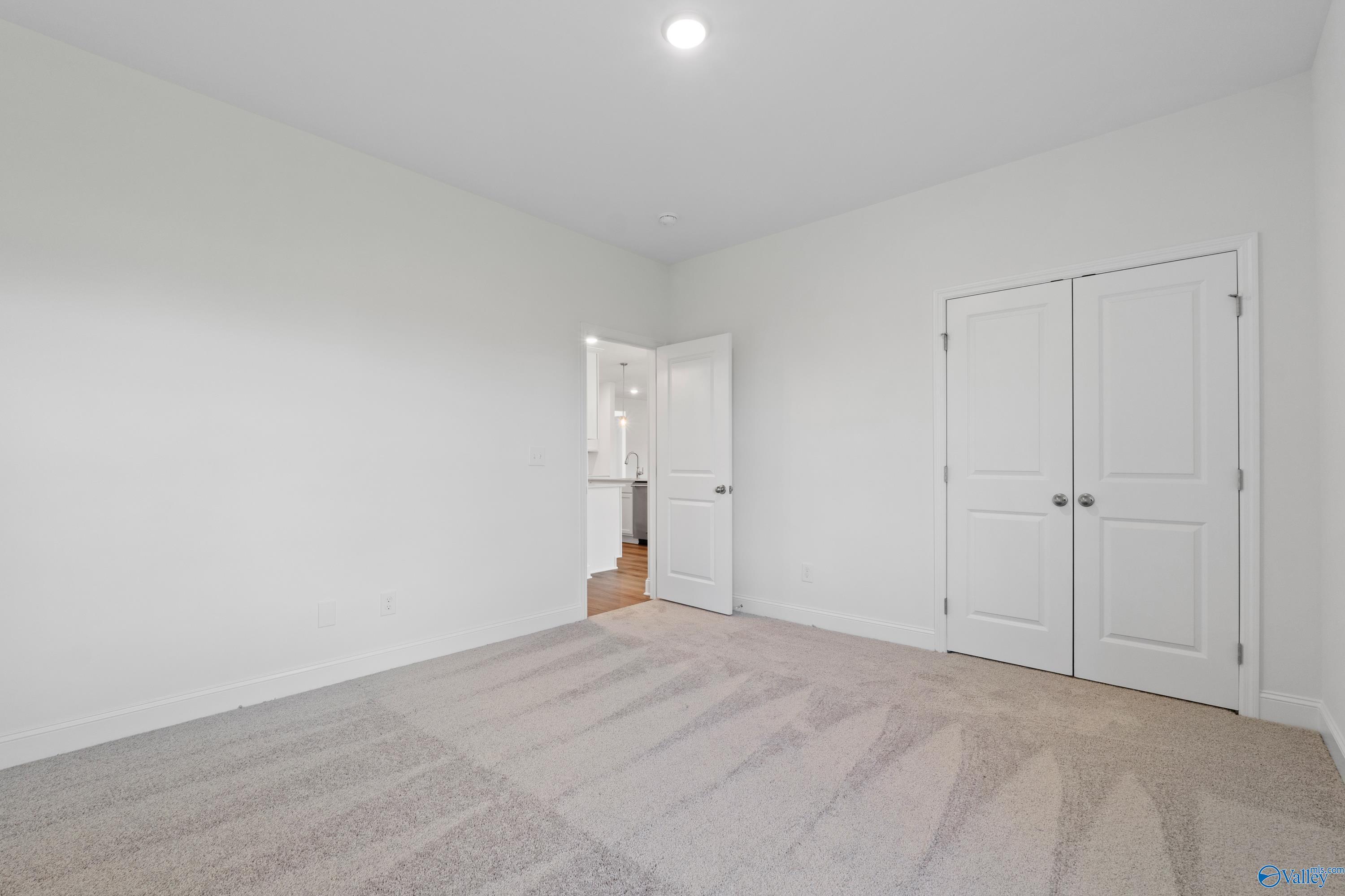 Spacious bedroom with white walls, beige carpet, double closet doors, and en-suite bath access in Davidson Homes The Oxford, Harvest, AL