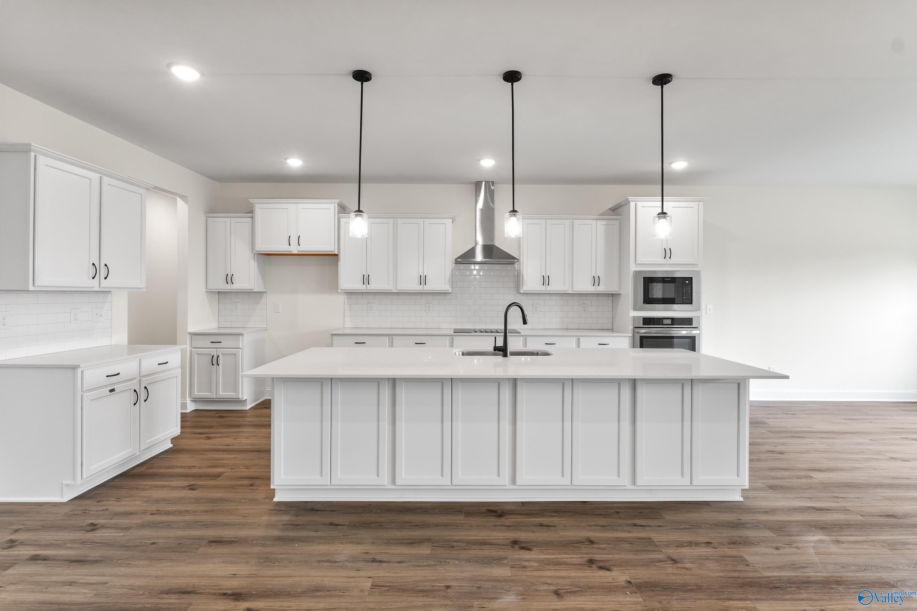 Modern white kitchen with large island, stainless appliances, pendant lights in Davidson Homes The Finleigh, Harvest, AL