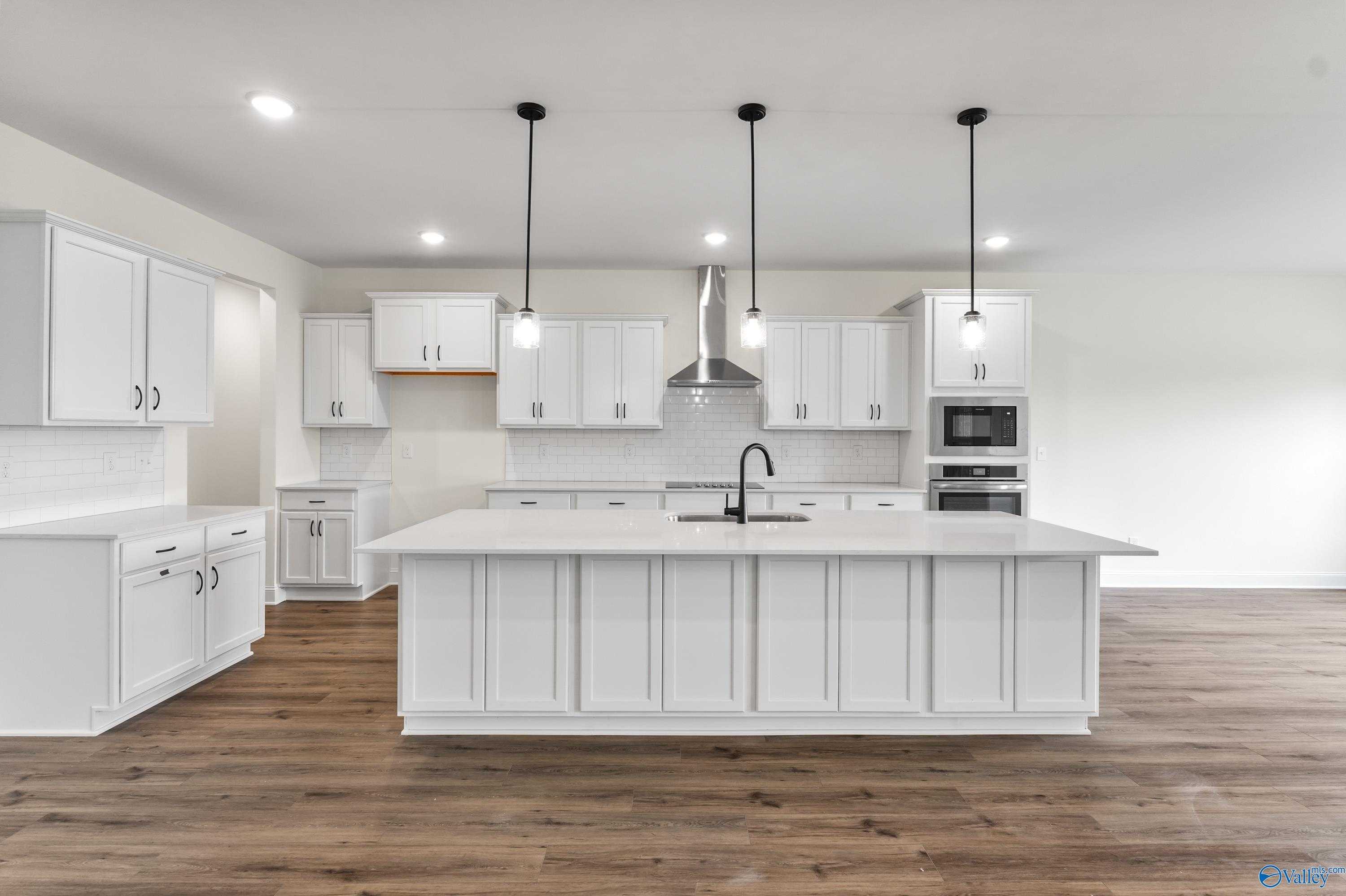 Modern white kitchen with large island, stainless appliances, pendant lights in Davidson Homes The Finleigh, Harvest, AL