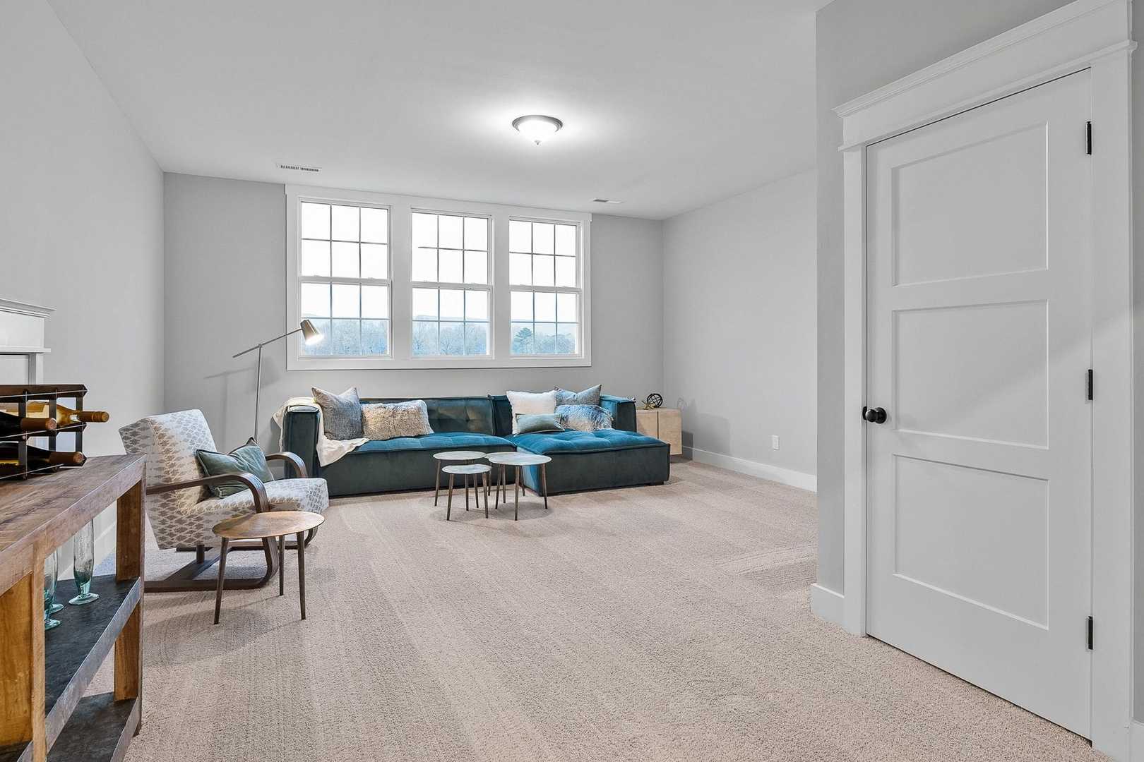 Spacious bonus room in The Oxford home design with teal sofa, wooden toy shelves, and large windows