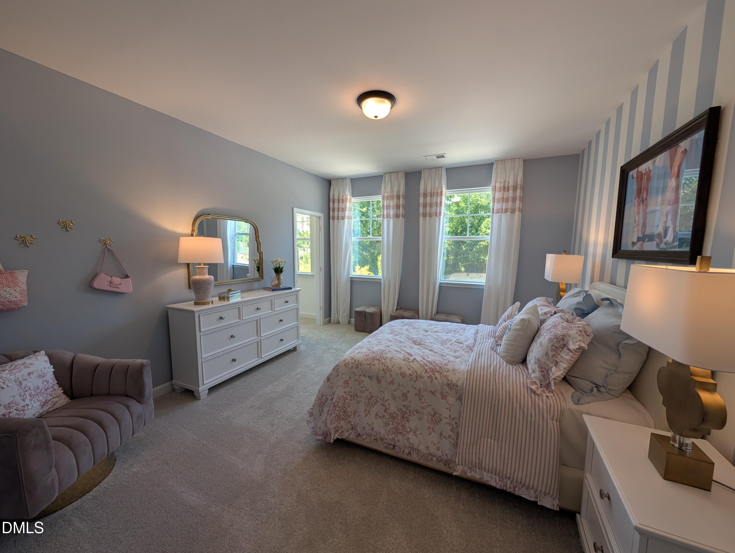 Cozy bedroom with striped wallpaper and floral bedding in The Aspen B floor plan at Wendell Ridge, Wendell, North Carolina.