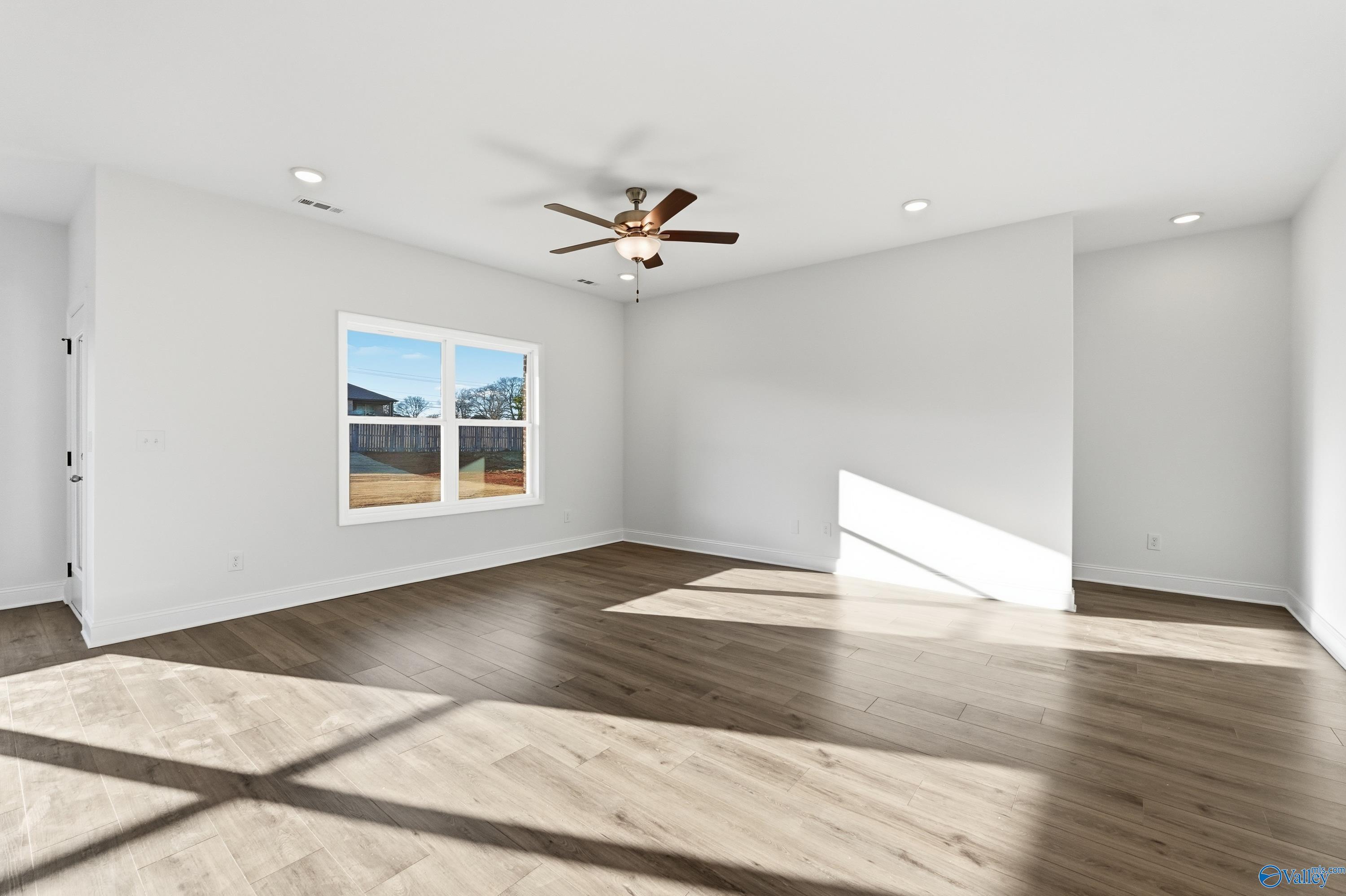 Bright bedroom with light hardwood floors, ceiling fan, and large window in Davidson Homes The Asheville C, Meridianville, AL