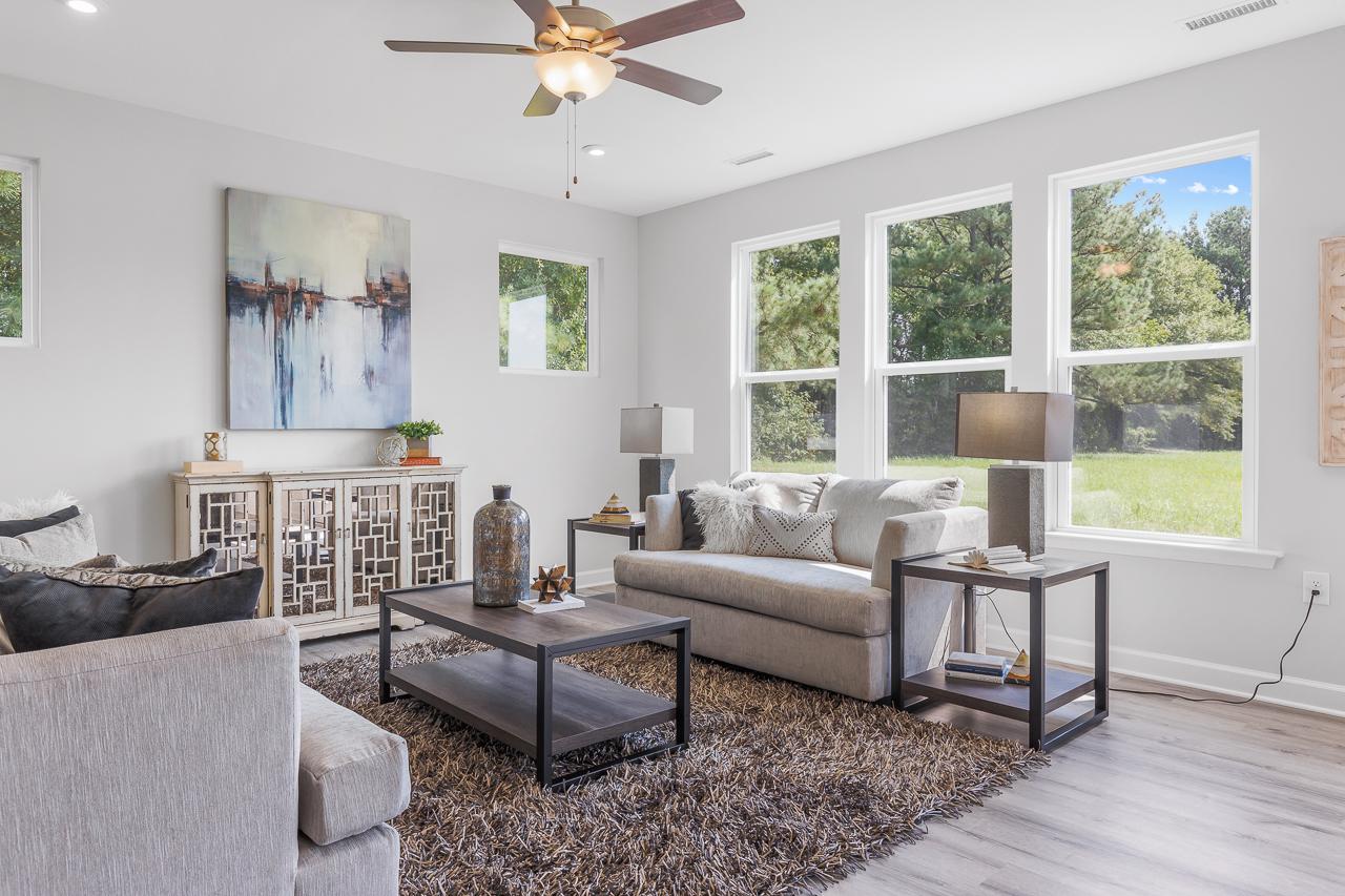 Spacious living room in Stagecoach Corner Mebane NC featuring gray sofa large windows hardwood floors and modern abstract art by Davidson Homes