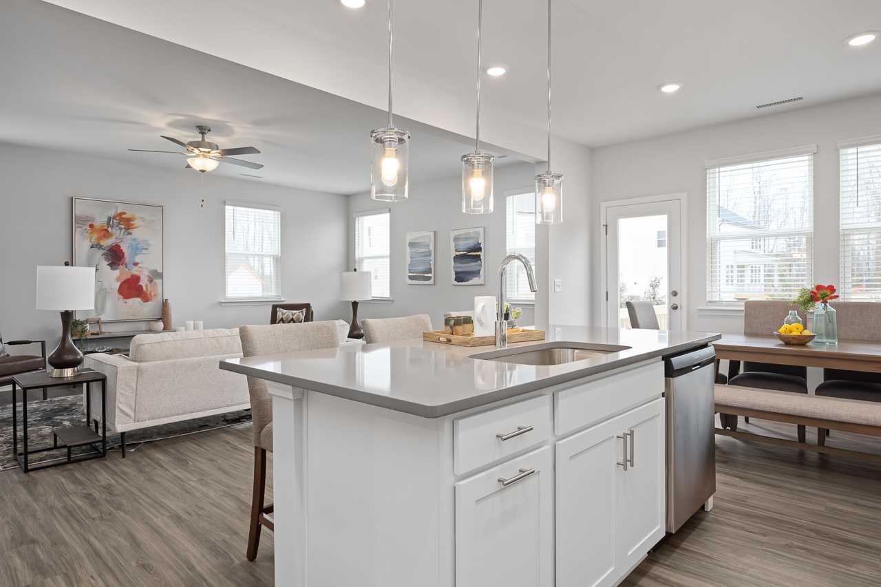 Open-concept kitchen and living area at Gregory Village in Lillington NC with white island, quartz counters, hardwood floors, and pendant lights