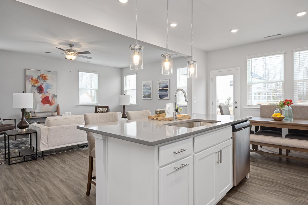 Open-concept kitchen and living area at Gregory Village in Lillington NC with white island, quartz counters, hardwood floors, and pendant lights
