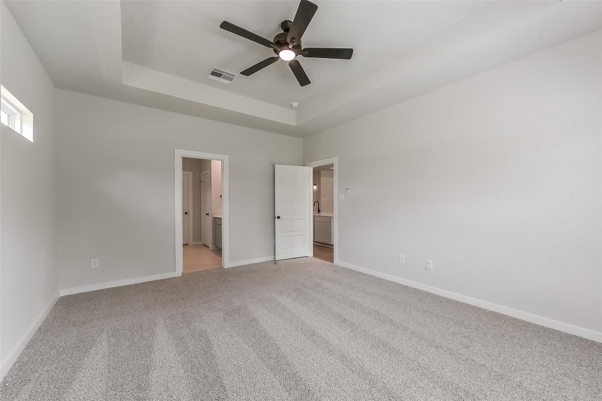 Spacious master bedroom with tray ceiling, dual ceiling fans, en-suite bath, and gray carpet in Davidson Homes Everett C, Crosby, Texas
