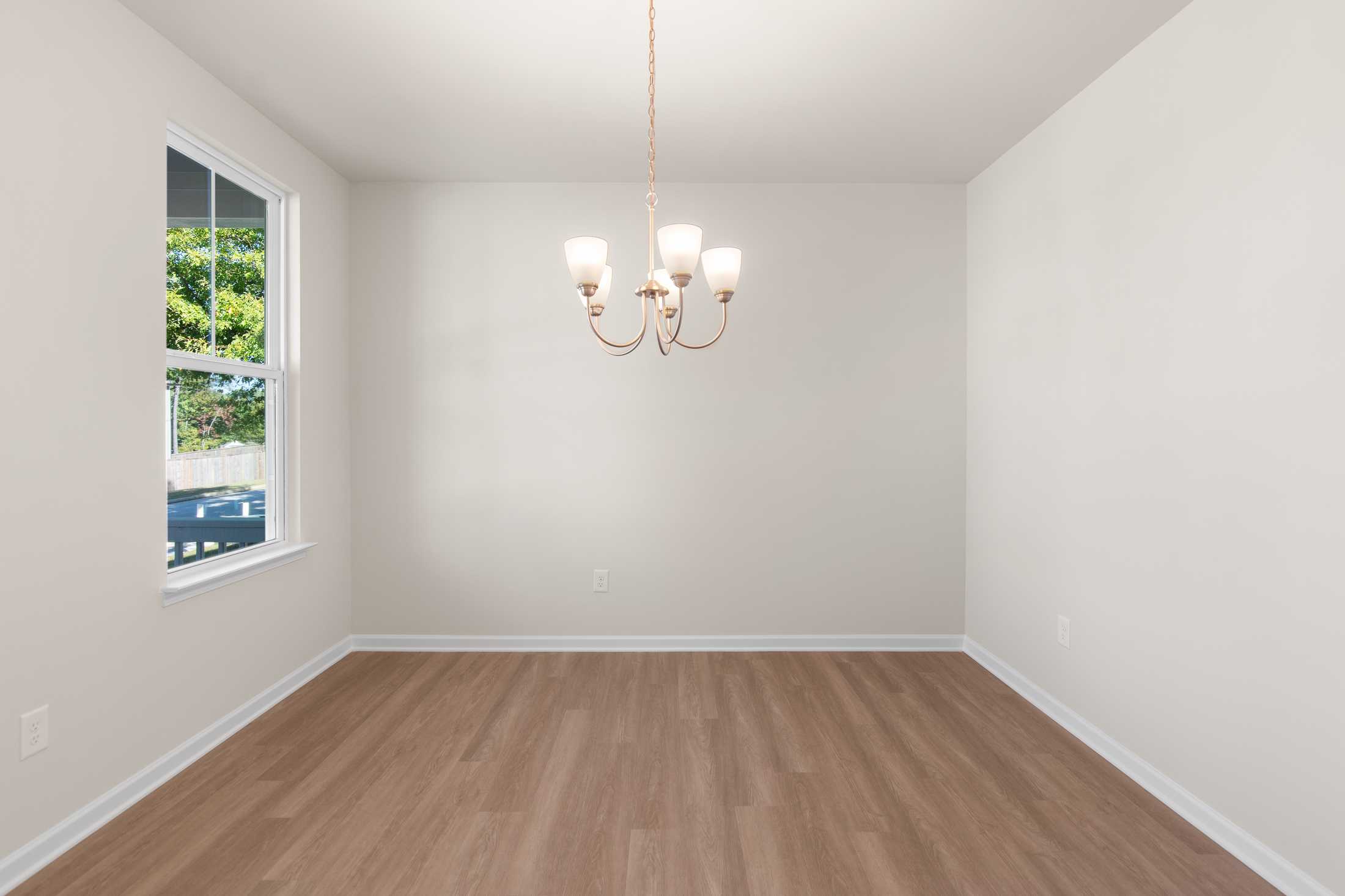 Bright dining room in The Willow B at Wehunt Meadows featuring elegant chandelier, large window with tree view, and hardwood floors