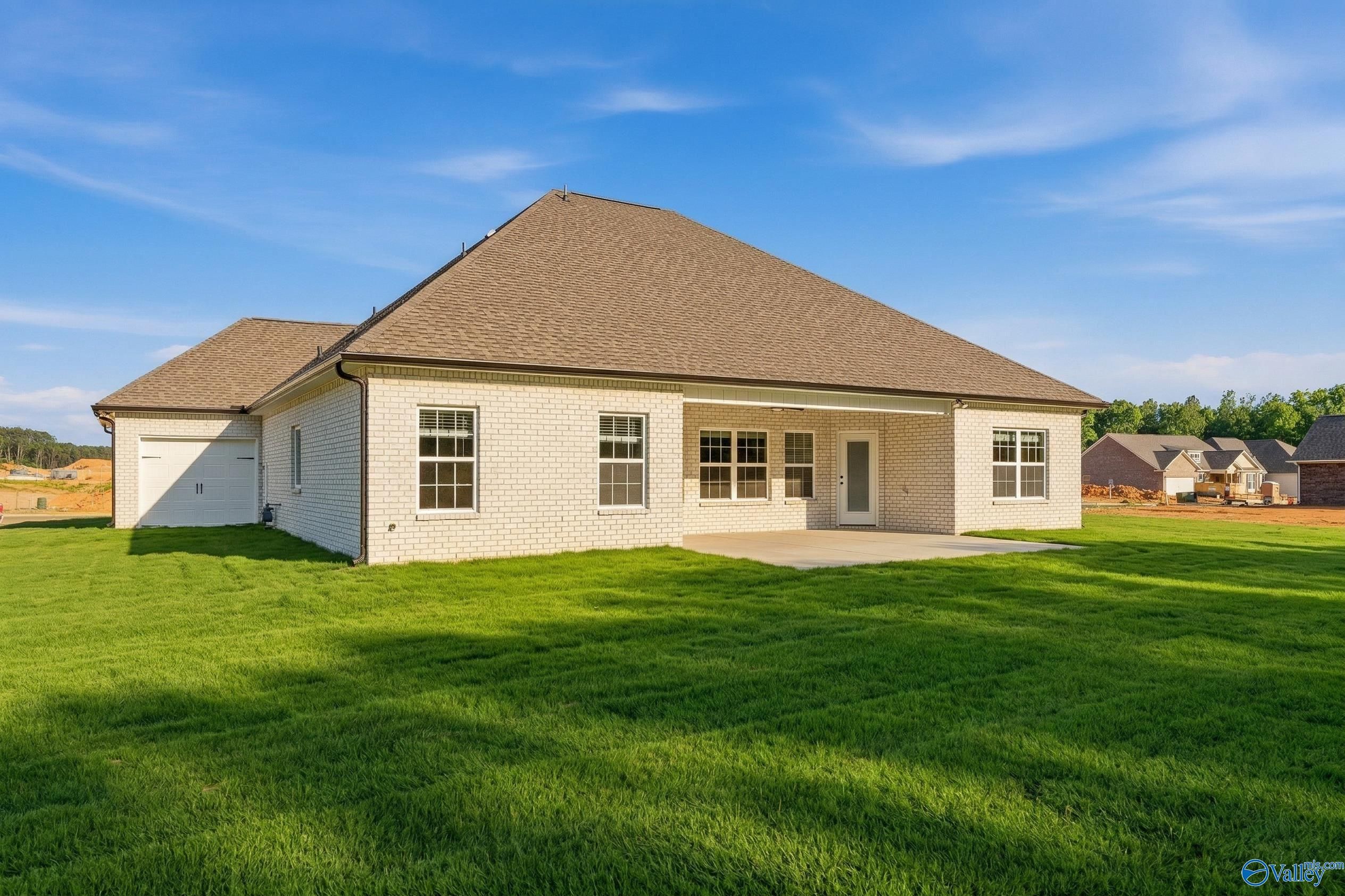 Rear view of brick The Rockford home with covered patio, 3-car garage, lush green lawn in Cain Park, Hartselle, Alabama