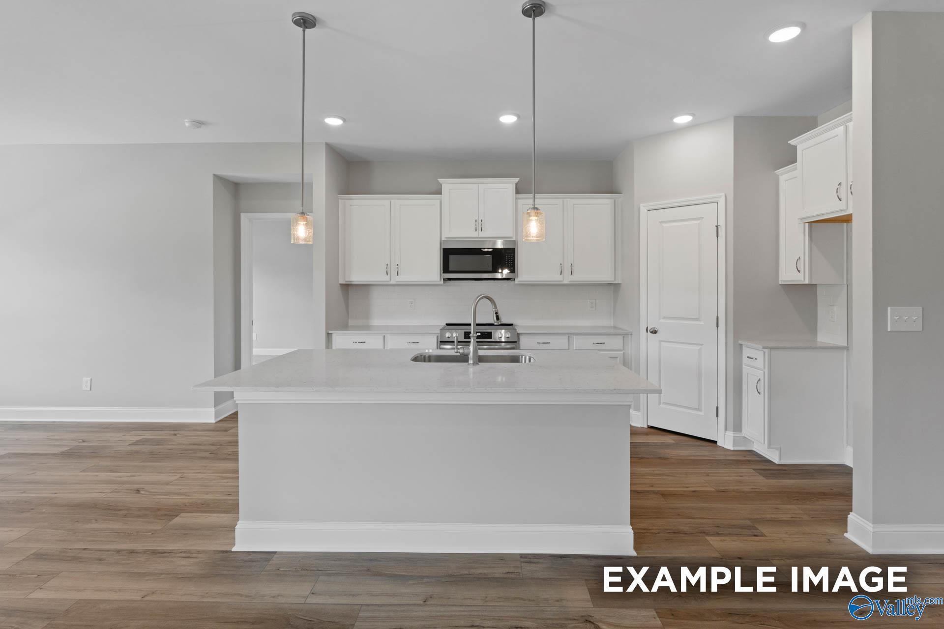 Bright modern kitchen with white shaker cabinets, quartz island sink, pendant lights, and hardwood floors in The Everett by Davidson Homes