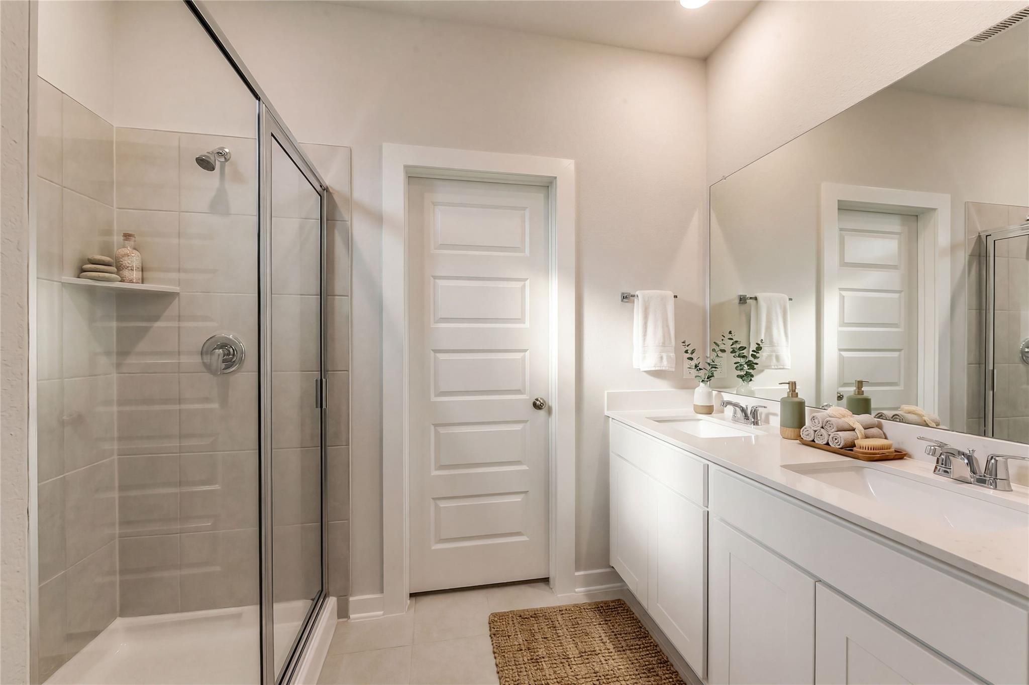 Modern master bathroom featuring glass walk-in shower, double white vanity, and eucalyptus decor in Davidson Homes The Brazos E, Dayton Texas