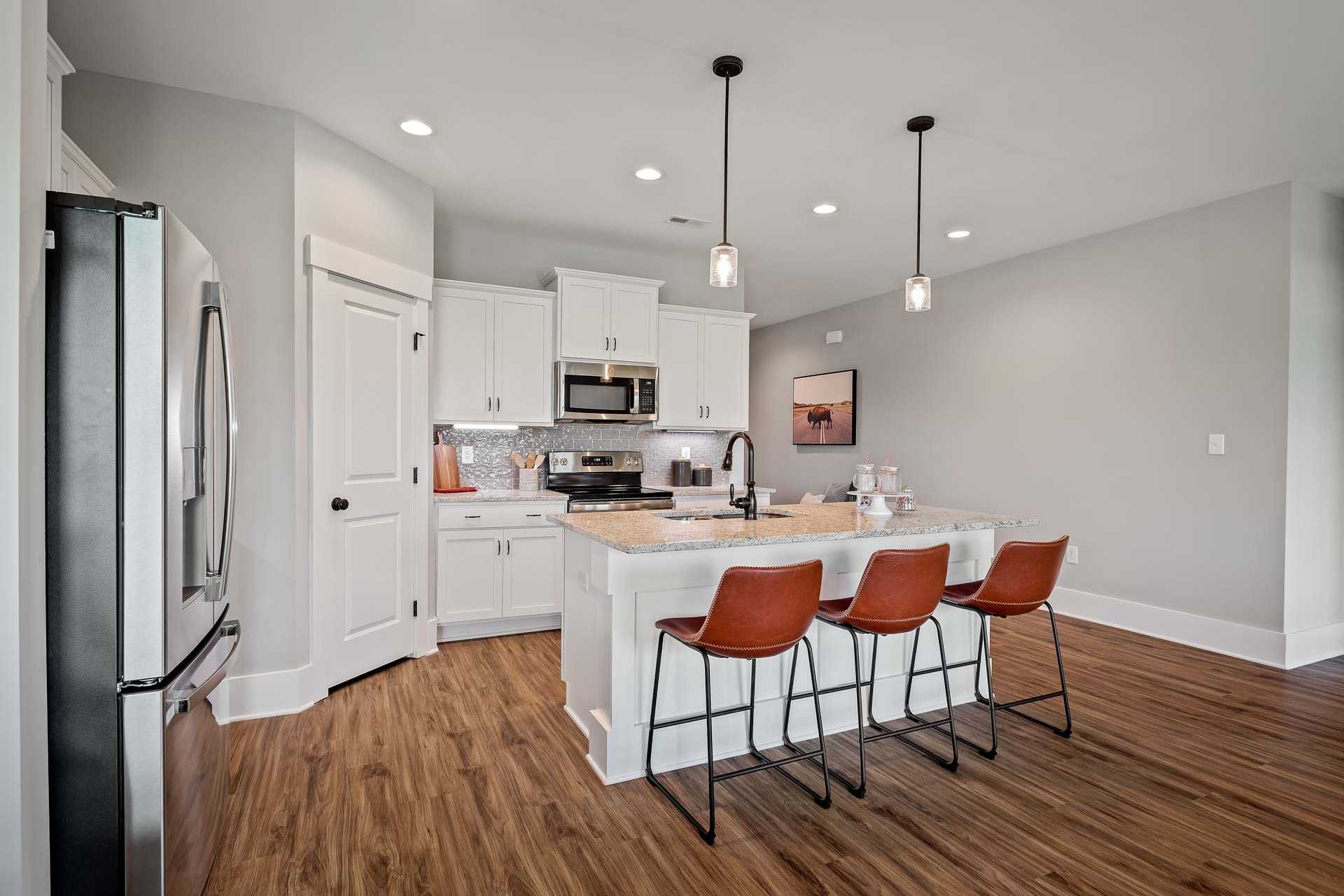 Bright kitchen at Heritage Lakes in New Market AL with white cabinets, large island, orange bar stools, stainless appliances, hardwood floors