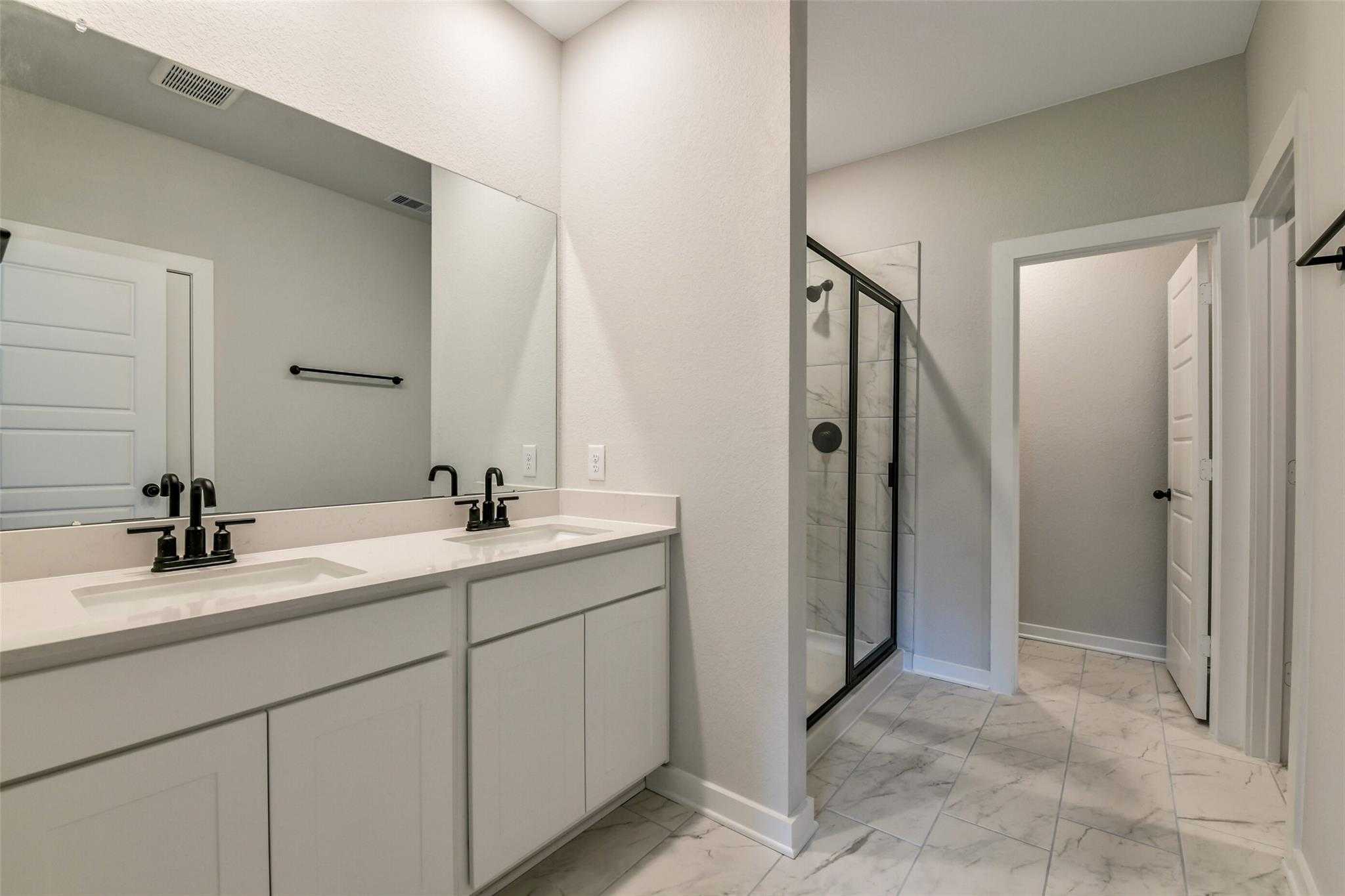 Modern master bathroom featuring double vanity sinks, frameless glass shower, and white cabinetry in Davidson Homes The Daphne H, Crosby, Texas