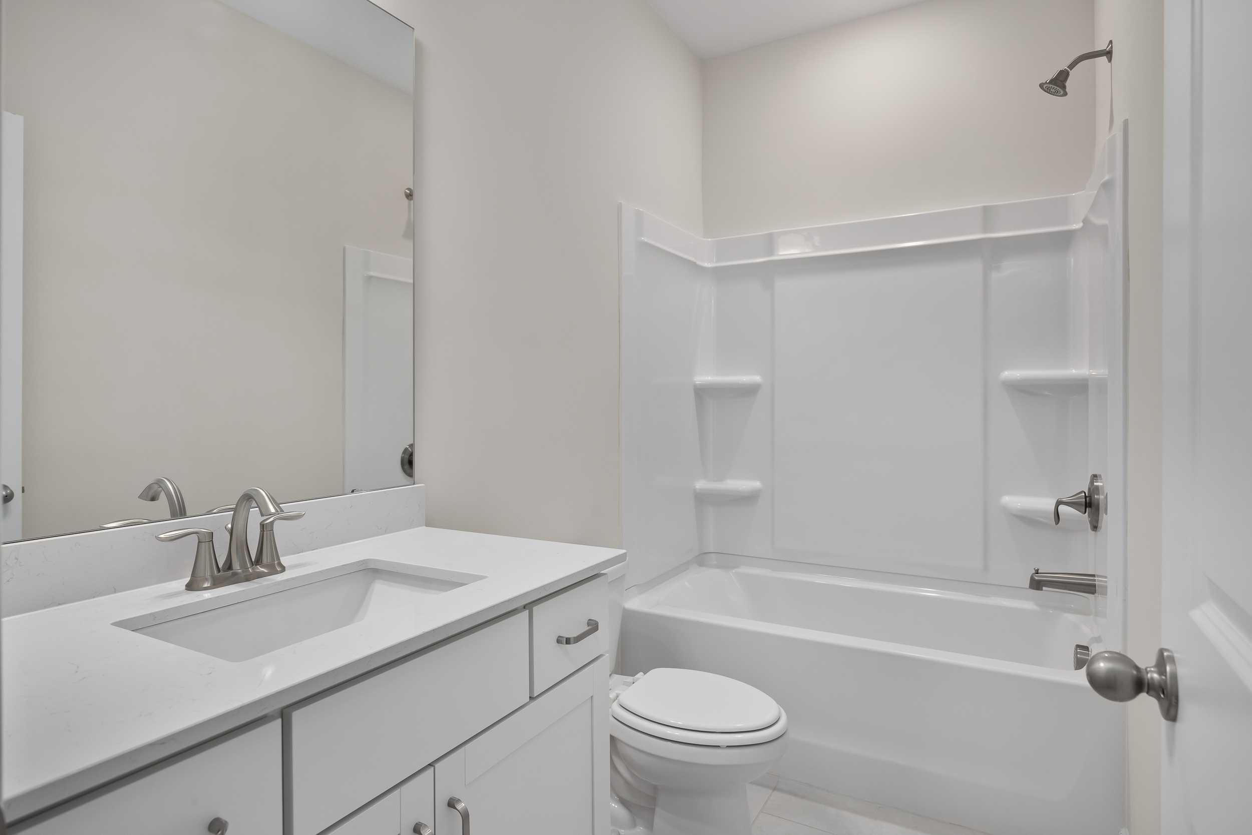 Modern secondary bathroom in The Beech C home design featuring white tub, corner shower, single vanity sink, and toilet