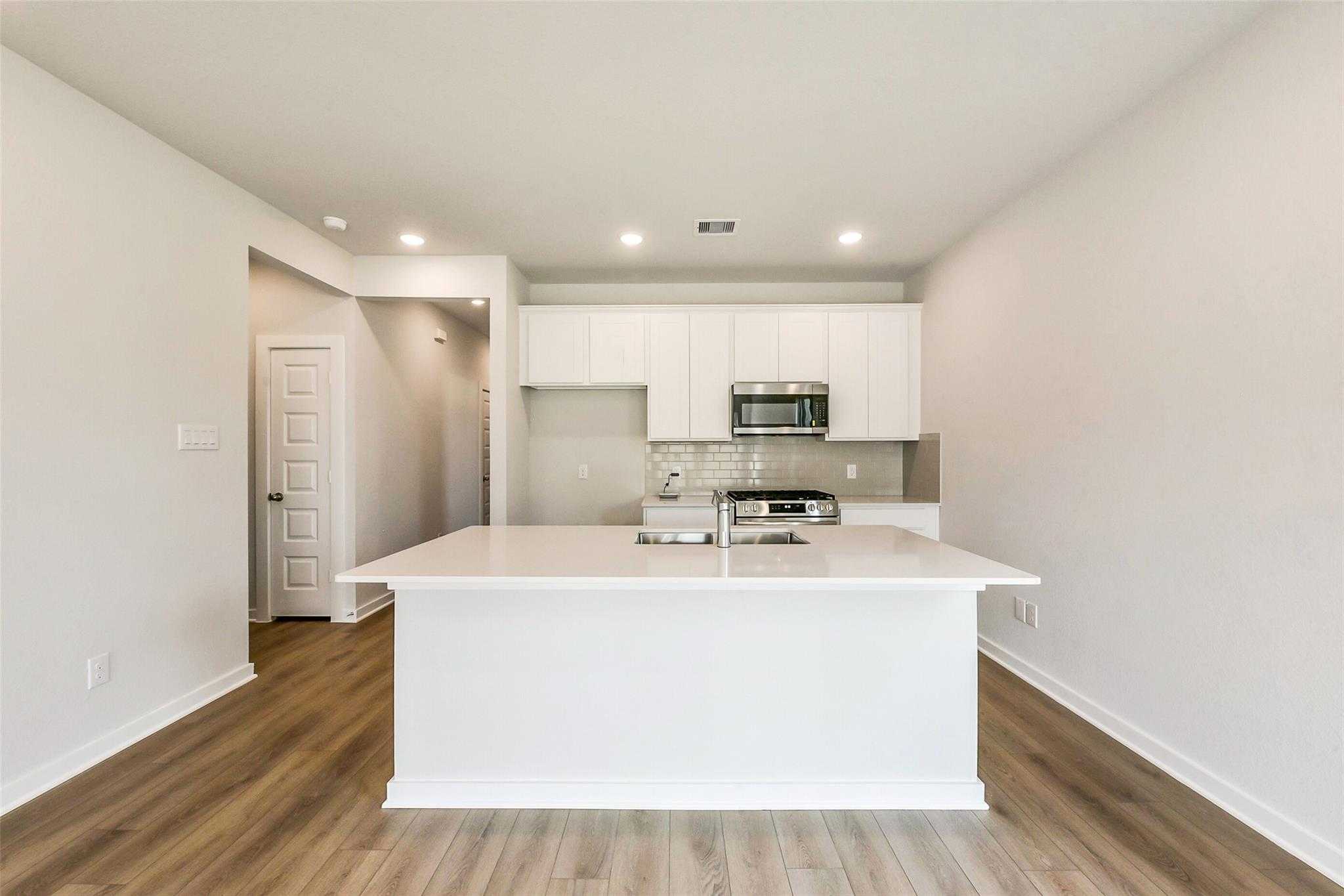 Modern white kitchen with large island, double sink, stainless appliances, and hardwood floors in Davidson Homes The Comal G, Dayton Texas