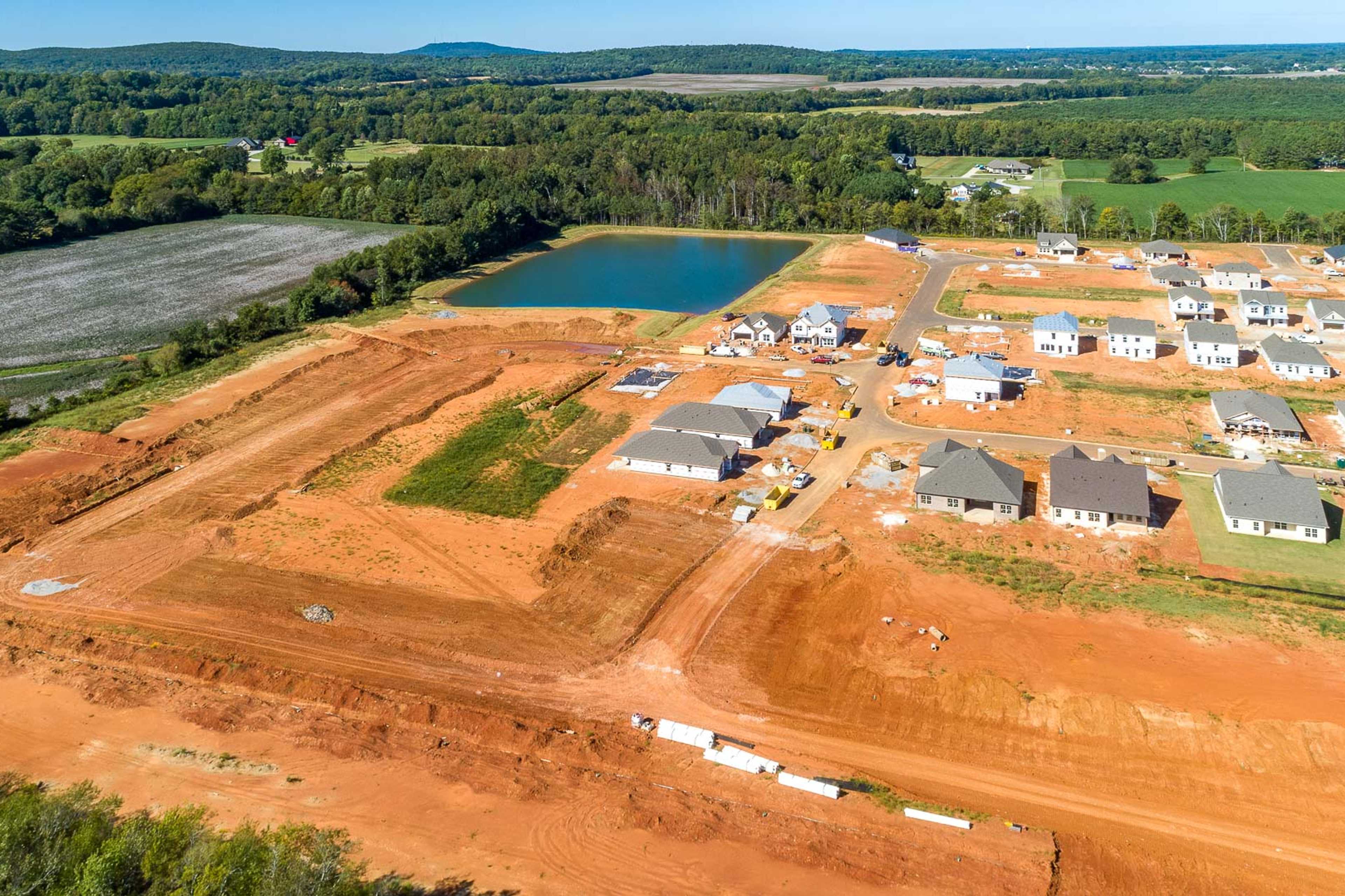 Aerial view of new homes under construction at Ivy Hills in Toney Alabama by Davidson Homes with pond and red dirt lots