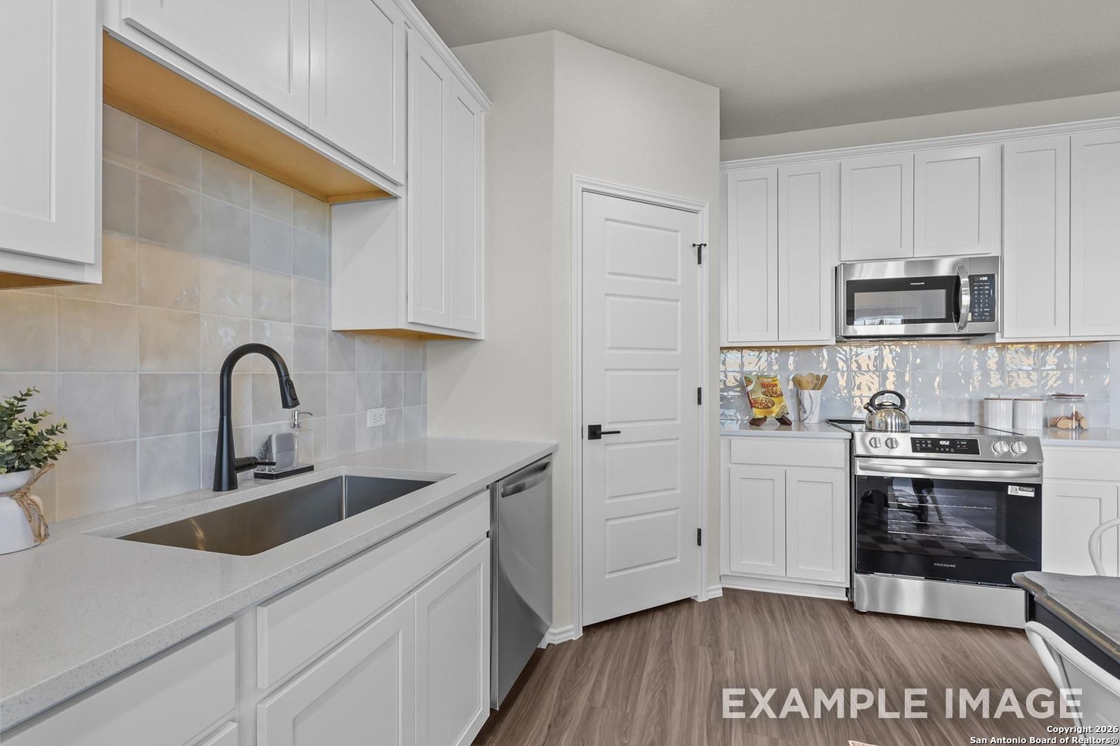 Modern white kitchen with stainless steel appliances, black faucet, and subway tile backsplash in Davidson Homes The Trinity B, San Antonio