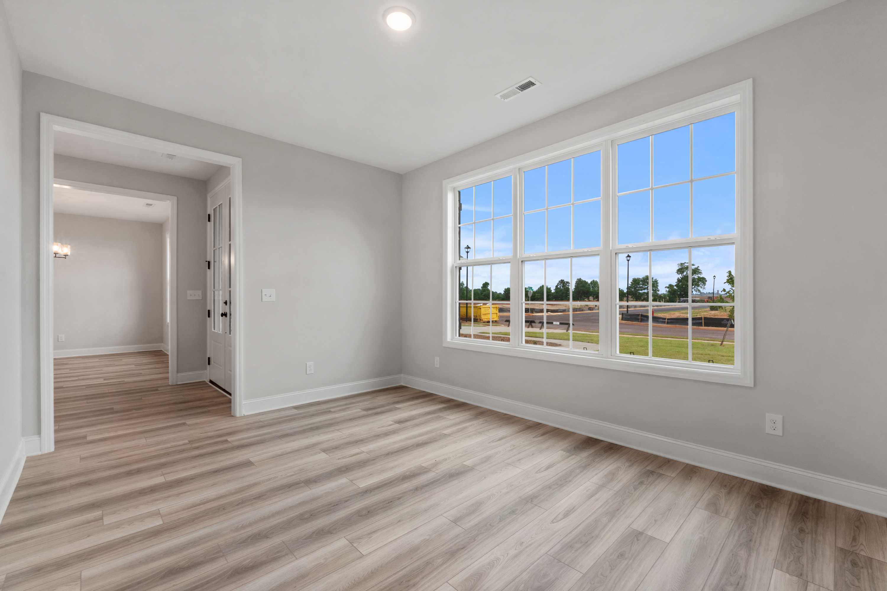 Spacious bedroom in The Oxford home design featuring light wood floors, gray walls, and large triple window with scenic green field view