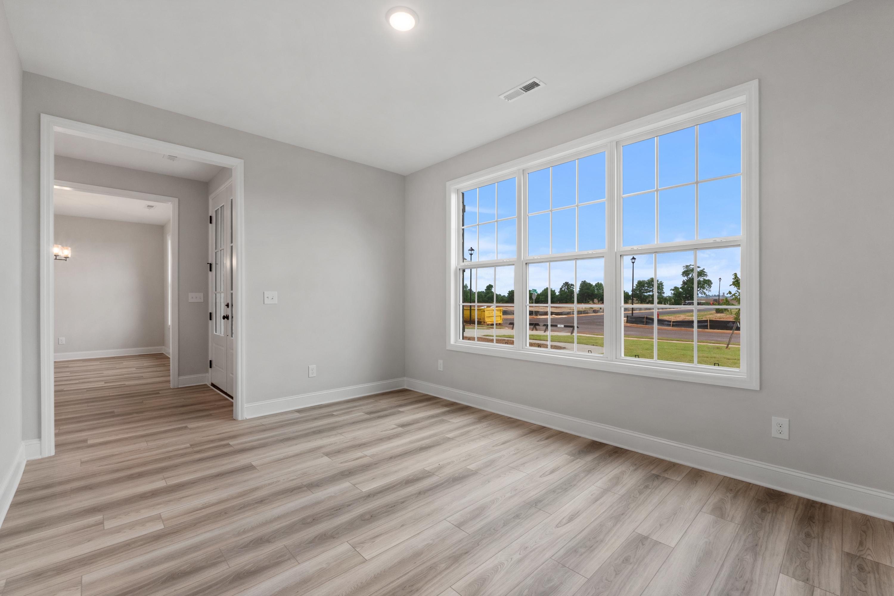 Spacious bedroom in The Oxford home design featuring light wood floors, gray walls, and large triple window with scenic green field view