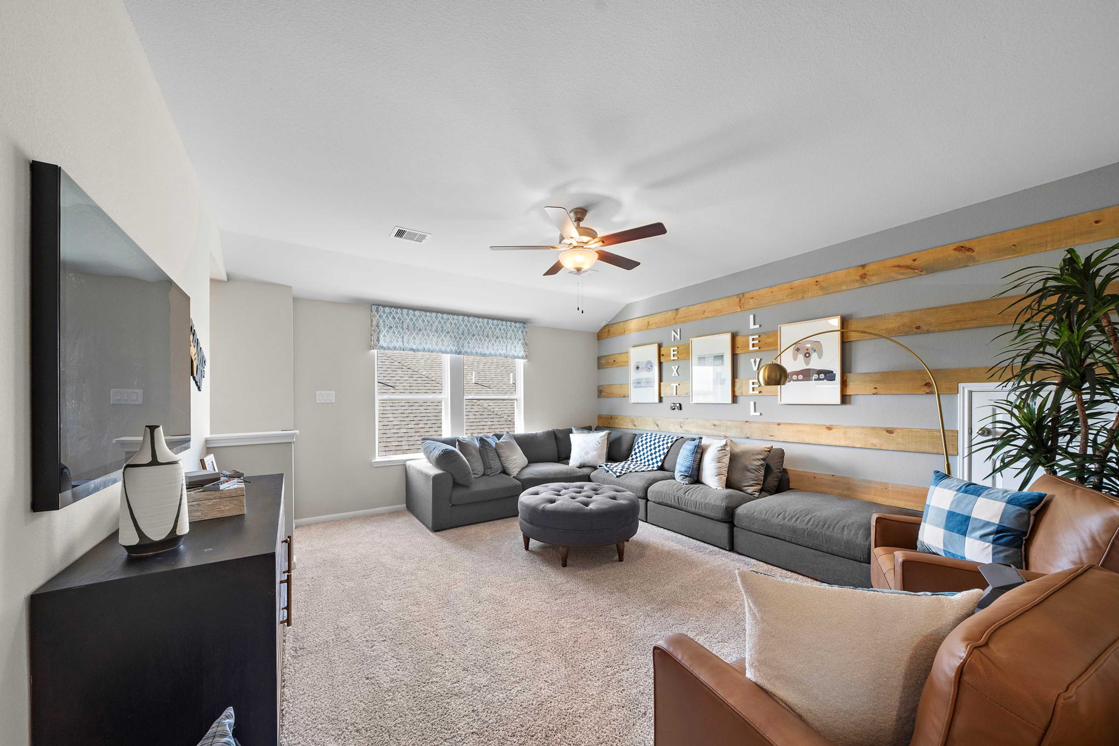 Cozy media room at Emberly in Beasley Texas featuring gray L-shaped sectional, wooden accent wall, mounted TV and ceiling fan