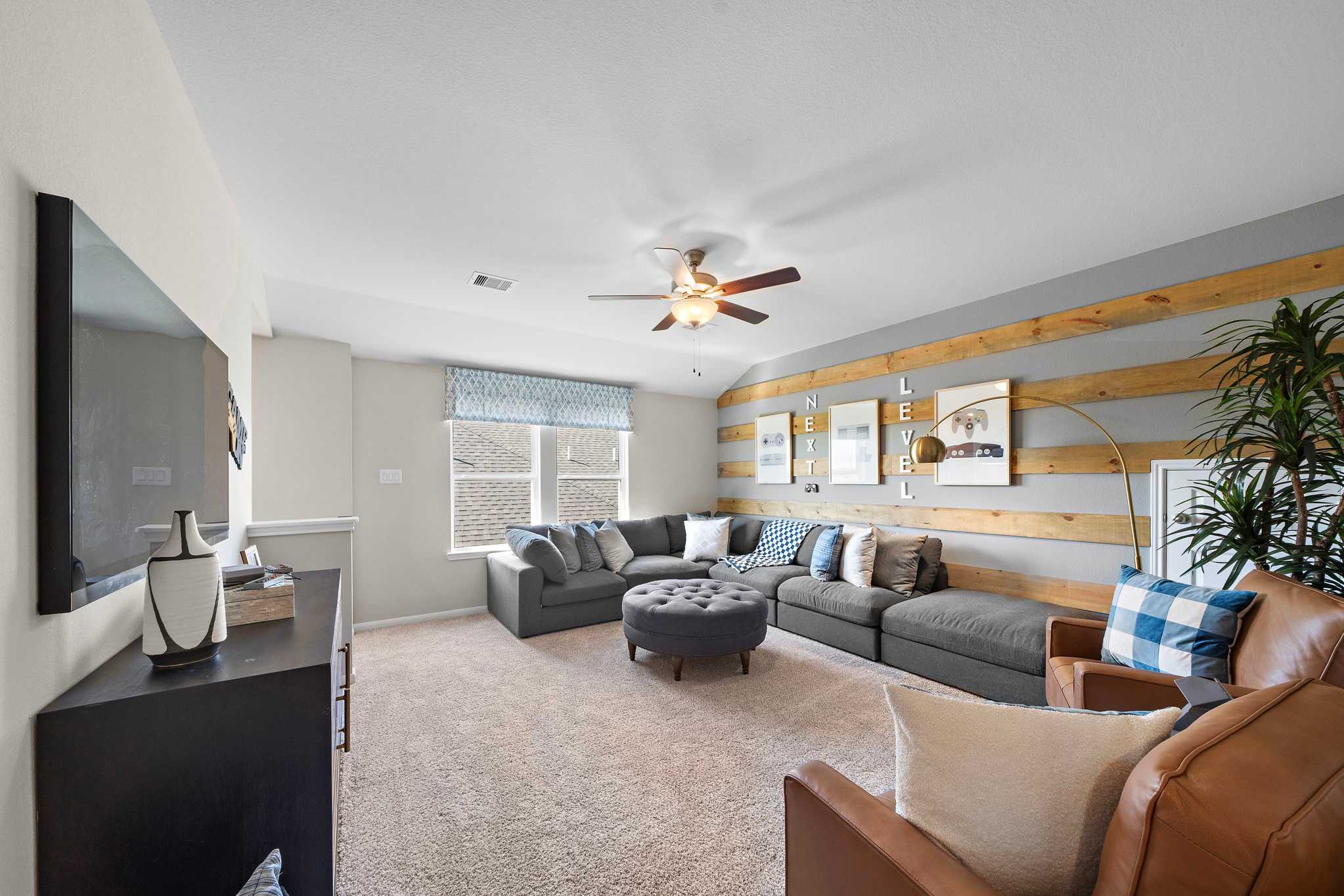 Cozy media room at Emberly in Beasley Texas featuring gray L-shaped sectional, wooden accent wall, mounted TV and ceiling fan