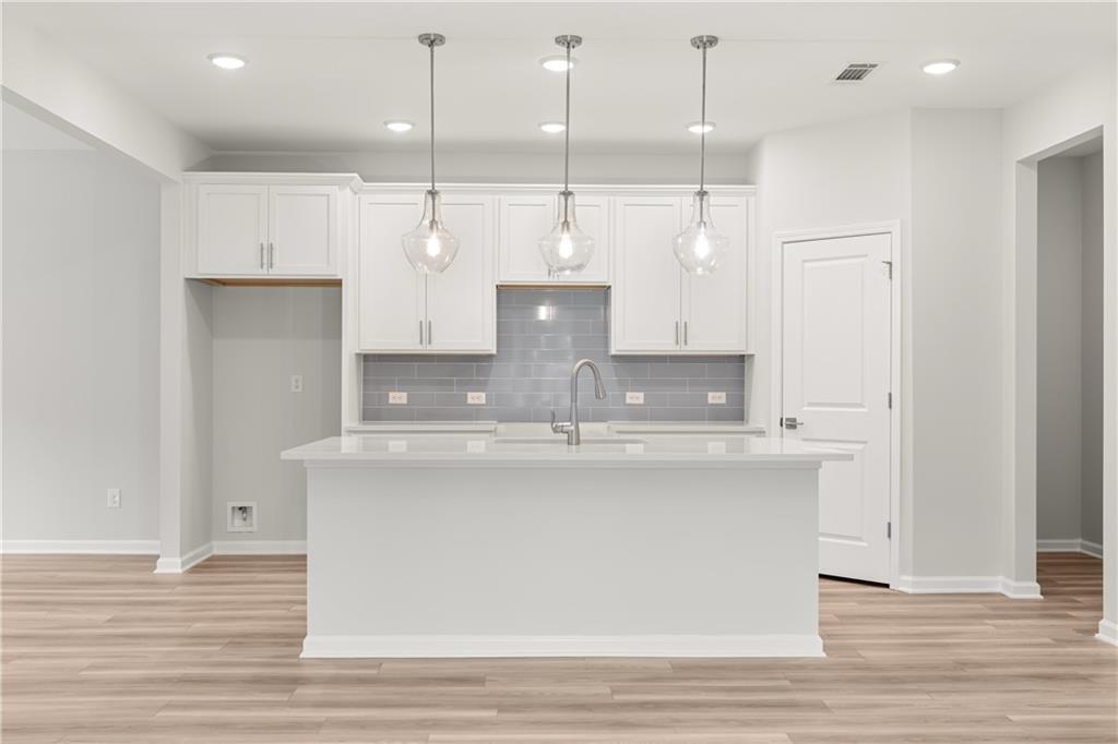 Modern kitchen with white cabinets, breakfast island, and gray subway tile backsplash in The Russell A at Cedar Farms.