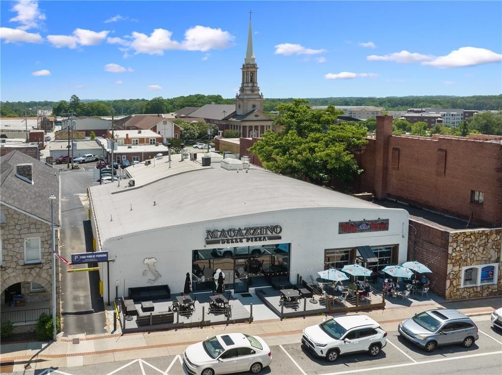 Aerial view of Magazzino Pizzeria with outdoor patio seating, umbrellas, parked cars, and historic church steeple in Loganville, Georgia