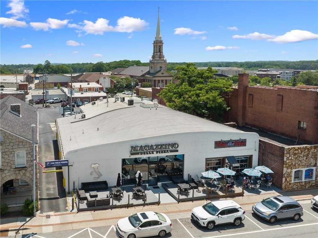 Aerial view of Magazzino building with Dolce Pera sign, outdoor patio seating under umbrellas, parked cars, and historic church steeple in Loganville, Georgia