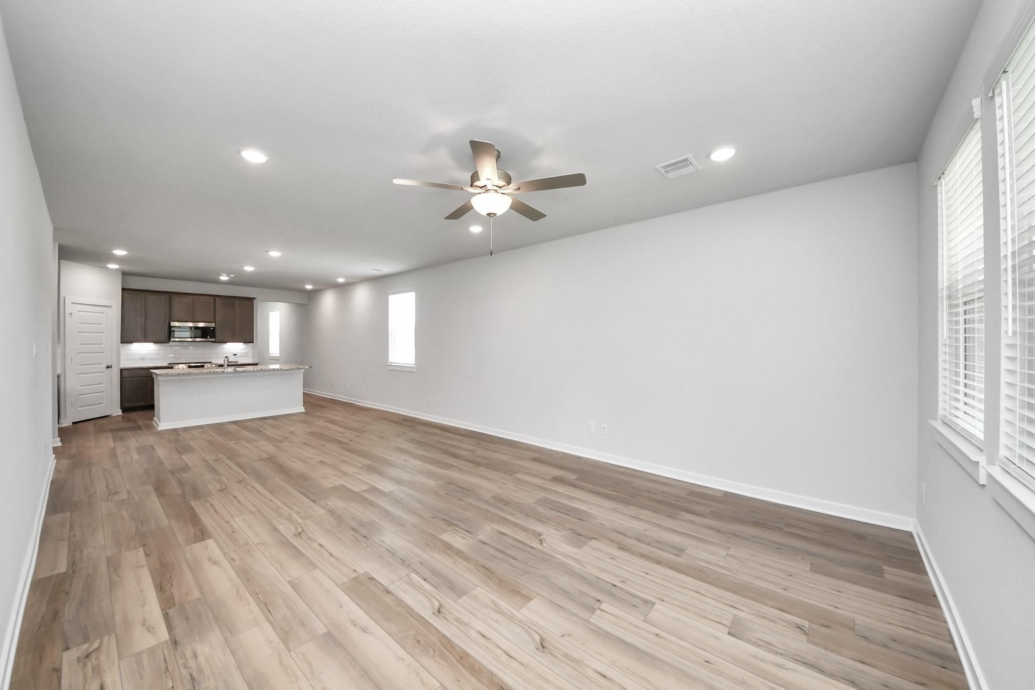 Spacious open-concept living area with wood-style flooring in The Sabine E floor plan at Liberty Estates, Cleveland, Texas.