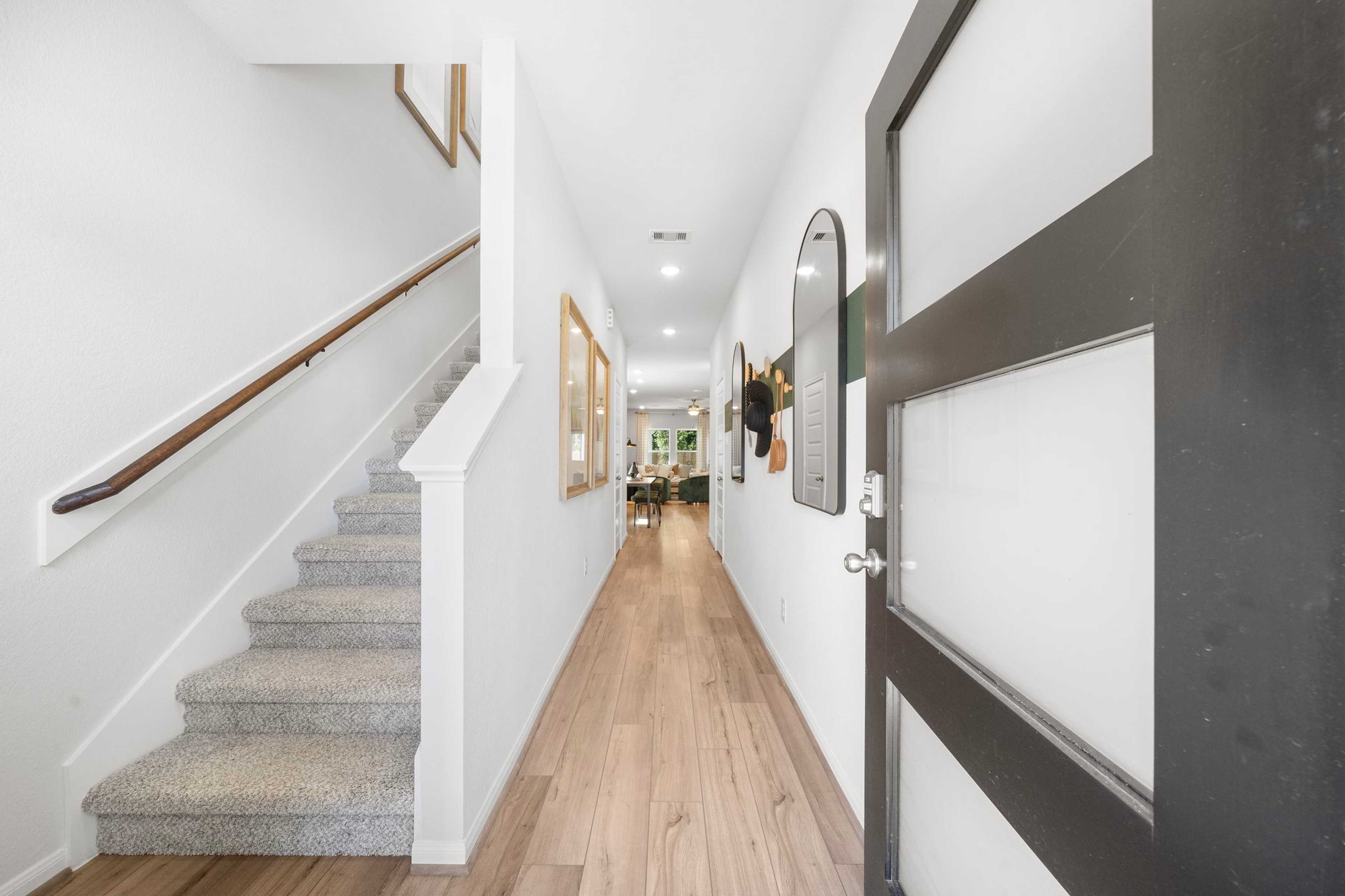Spacious modern hallway with oak hardwood floors, white walls, and carpeted staircase at Caney Creek Place in Conroe, Texas
