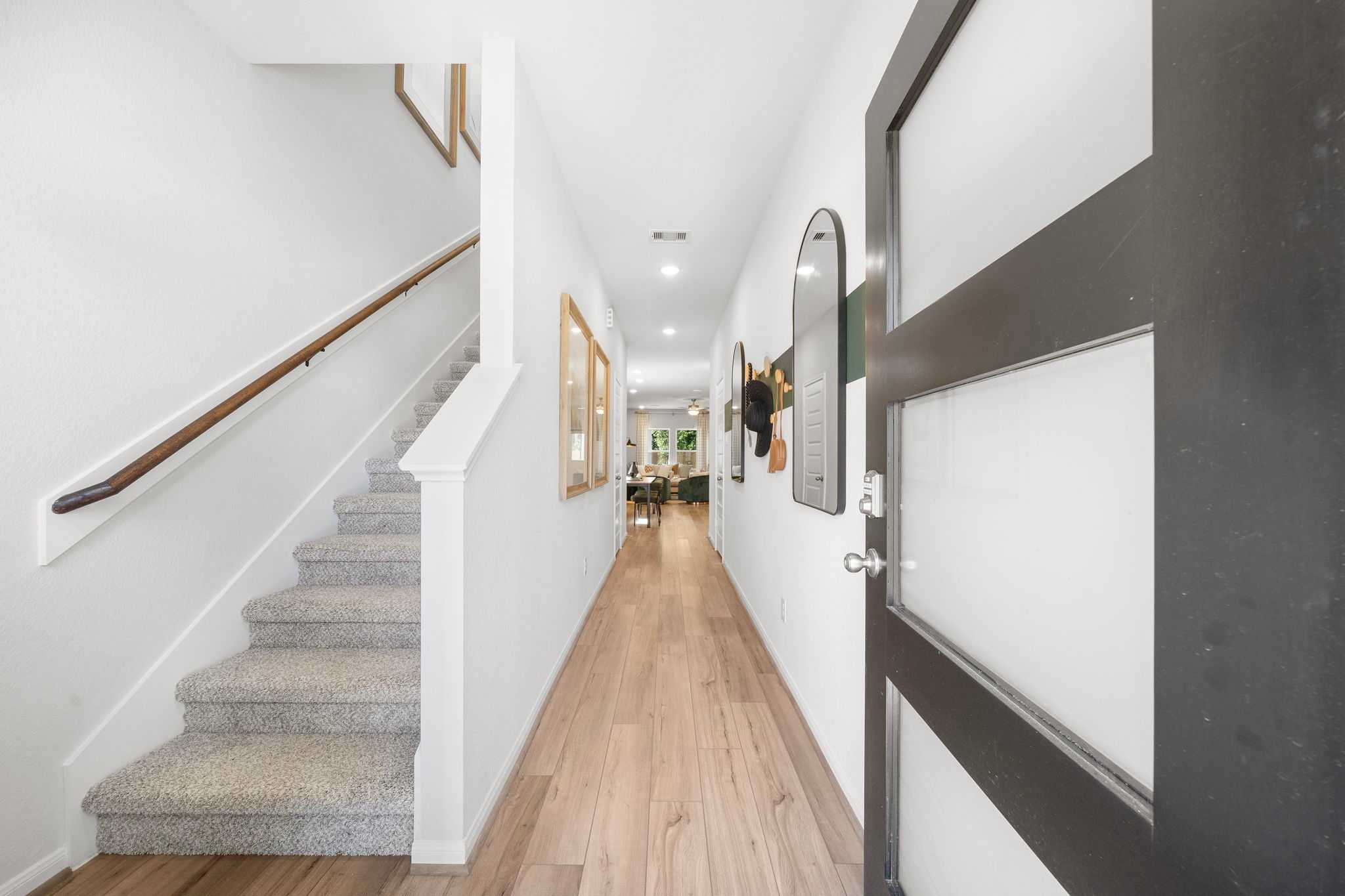 Spacious modern hallway with oak hardwood floors, white walls, and carpeted staircase at Caney Creek Place in Conroe, Texas