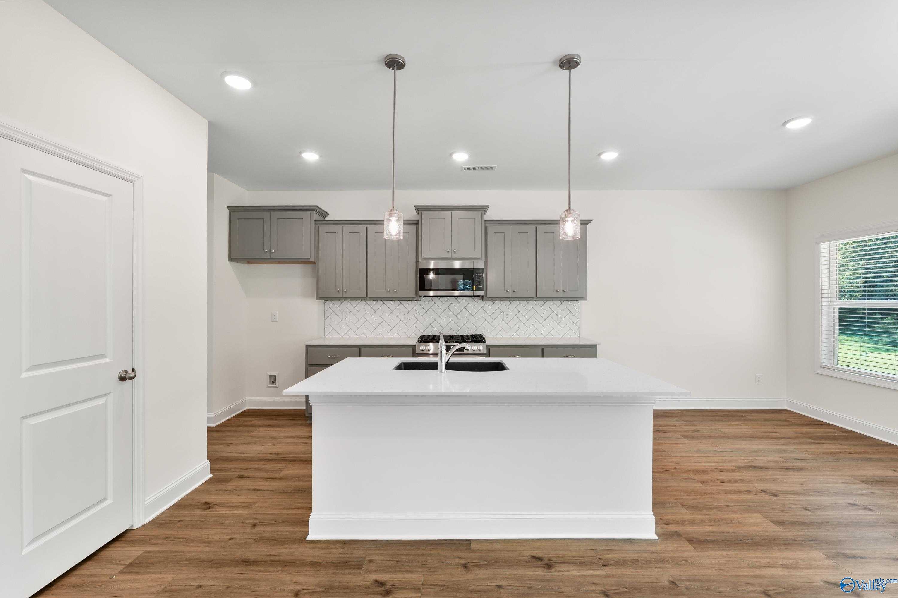 Modern kitchen with gray cabinets, white island sink, stainless microwave, subway tile backsplash in Davidson Homes The Shelby A, Athens AL