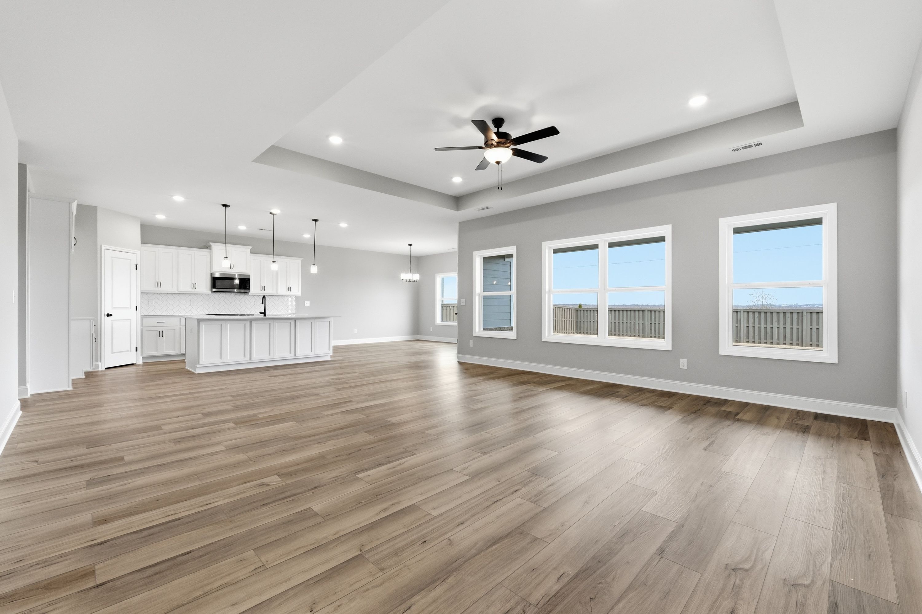 Spacious open-concept kitchen and living area in The Rockford featuring white cabinets, large island, hardwood floors, and large windows