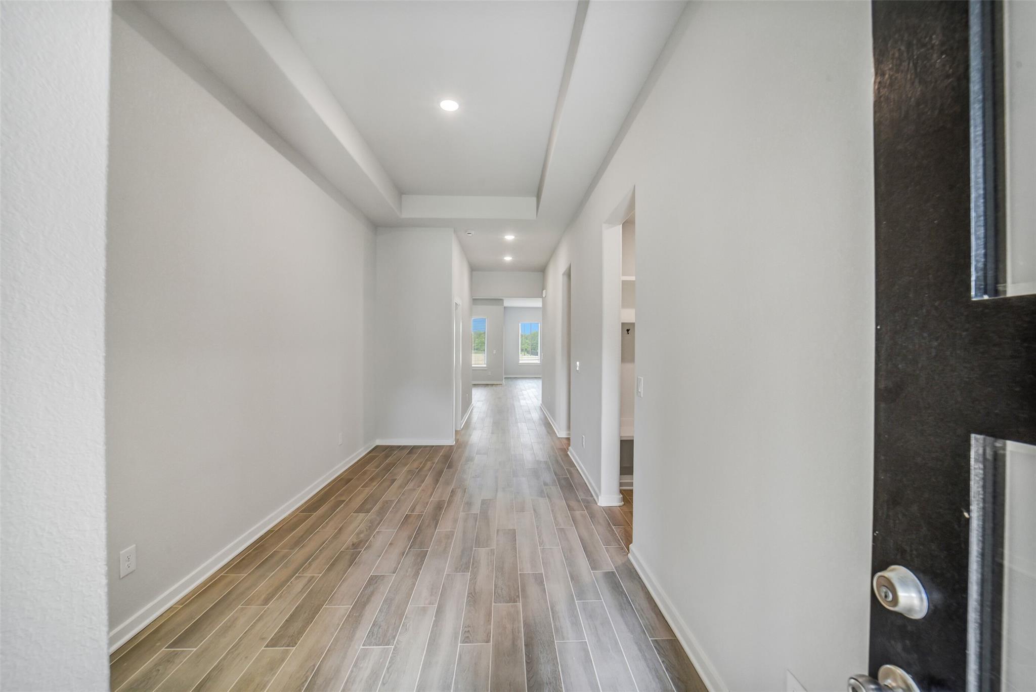 Spacious hallway with tray ceiling, recessed lights, and wood-look flooring in Davidson Homes The Acadia C, Magnolia Texas