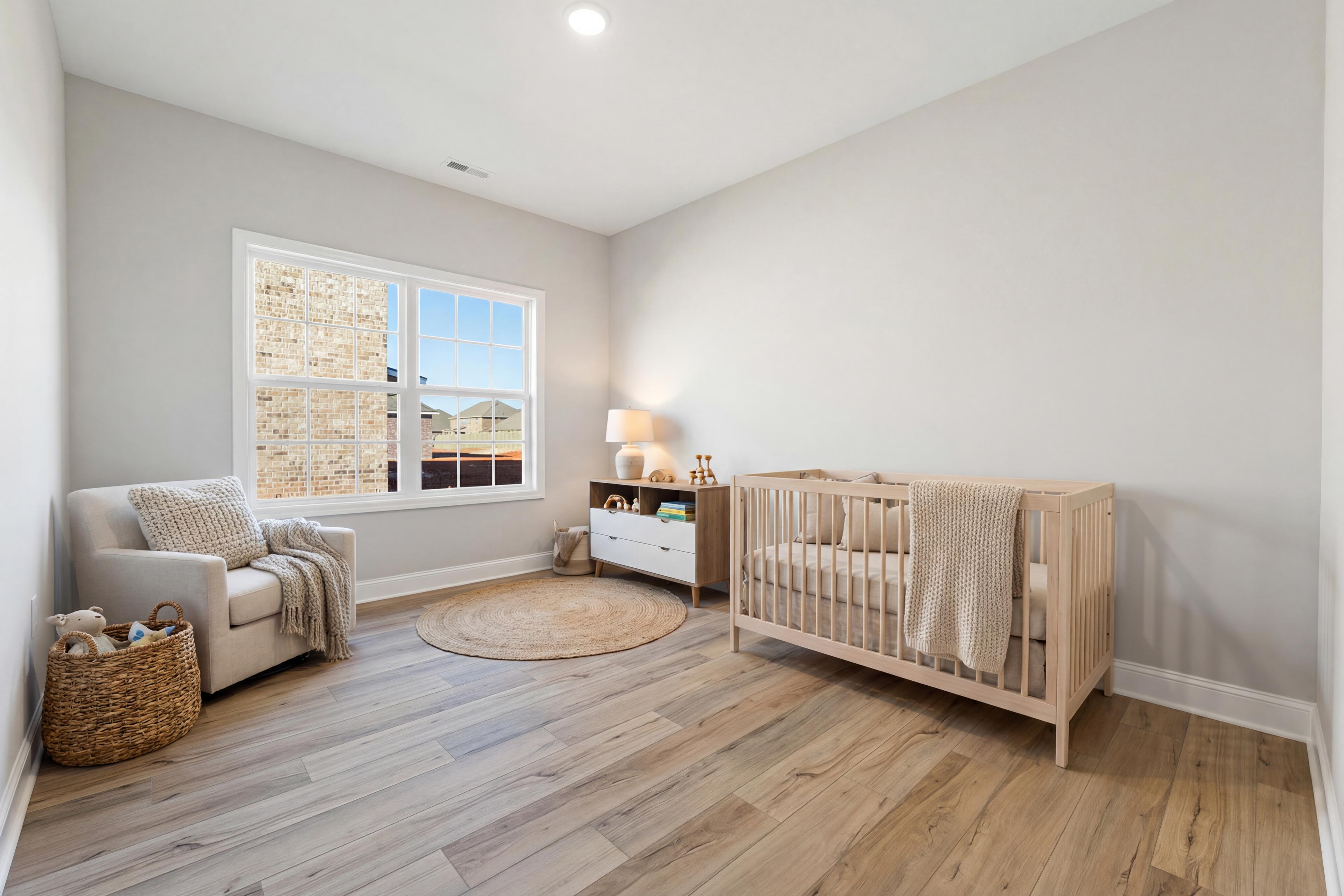 Cozy nursery in The Valencia home: white wooden crib with blankets, changing table, plush armchair, gray walls, hardwood floors