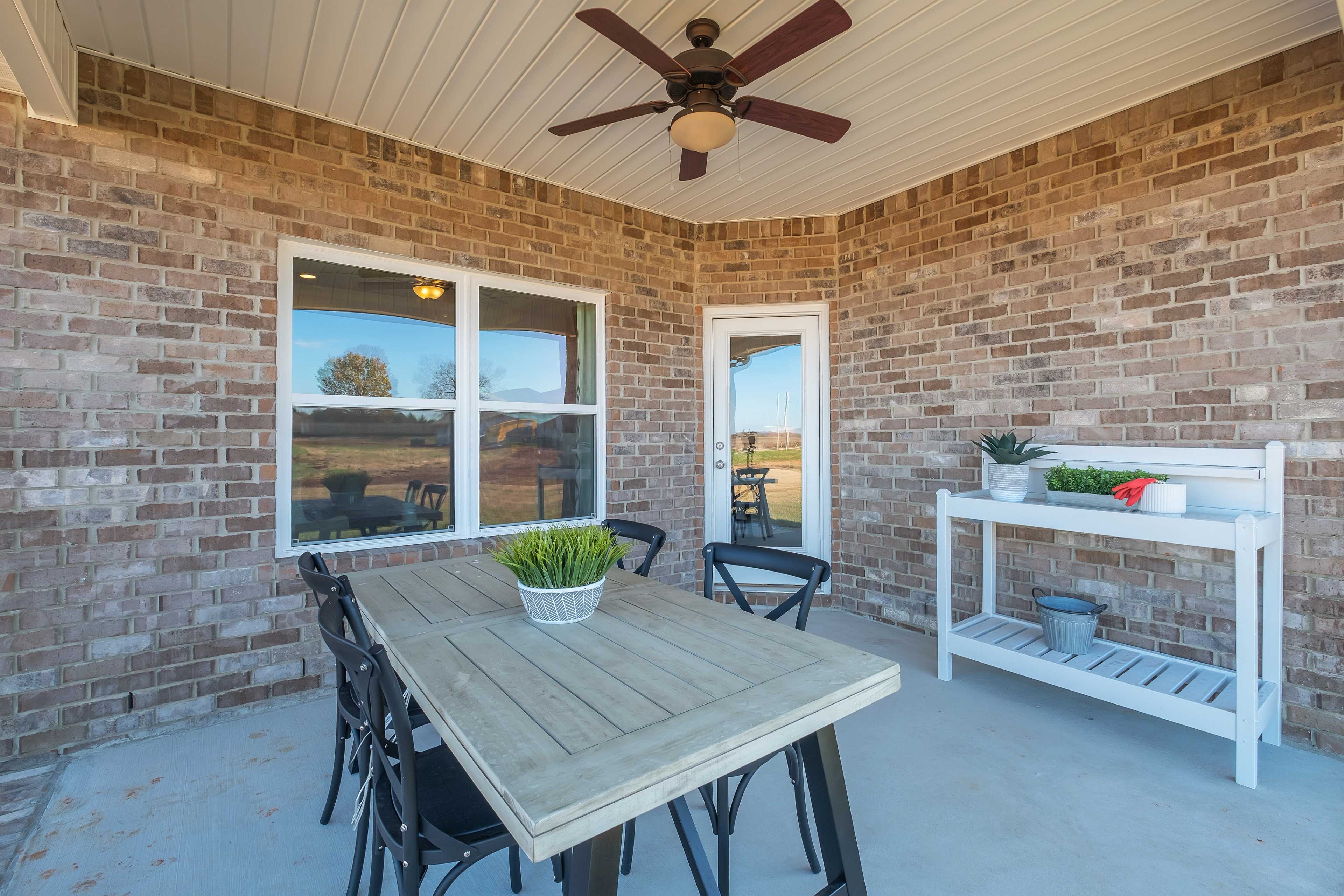 Covered patio at Mallard Landing in Athens AL featuring brick walls, ceiling fan, wooden dining table, black chairs, and potted plants