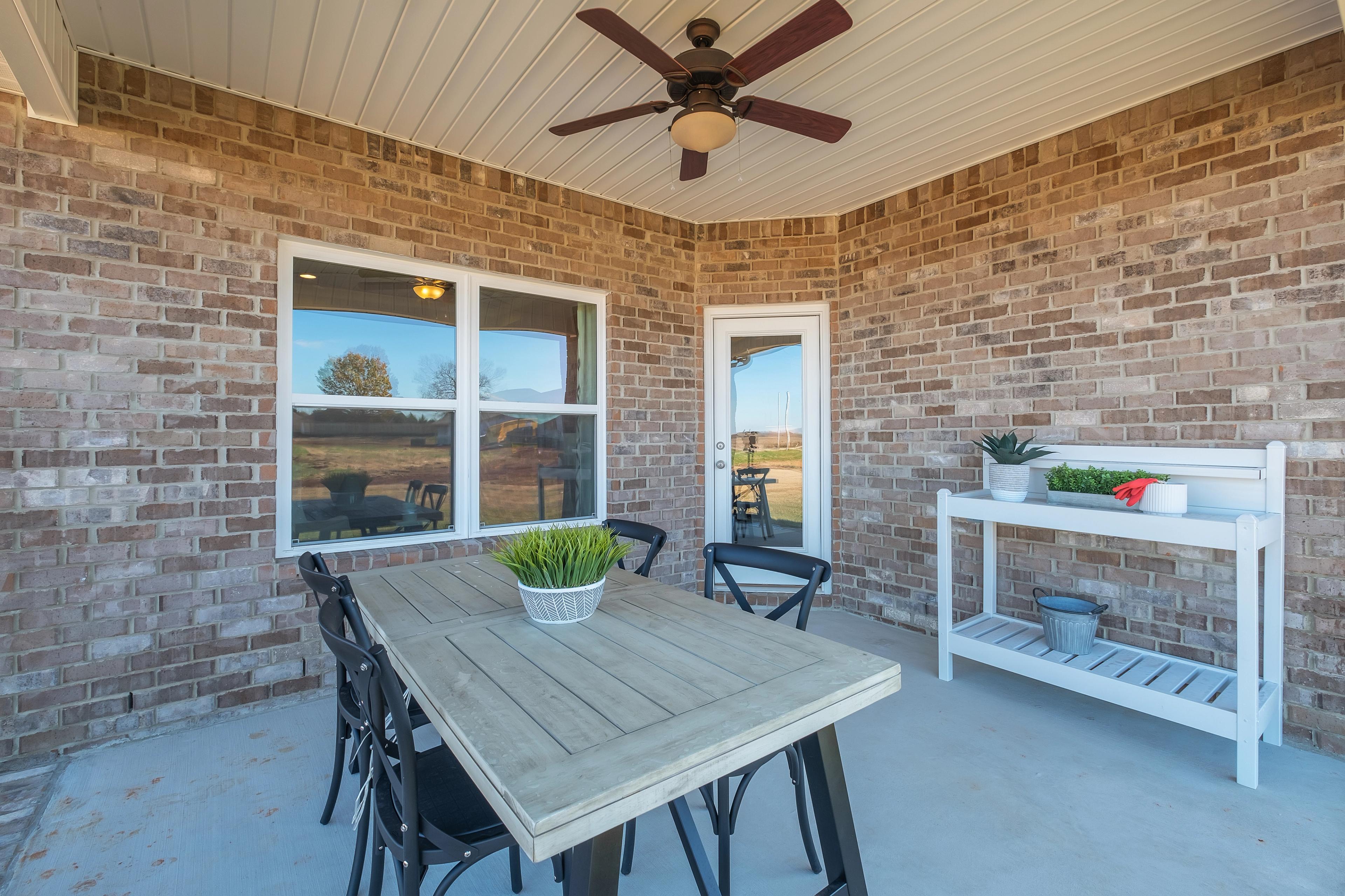 Covered patio at Mallard Landing in Athens AL featuring brick walls, ceiling fan, wooden dining table, black chairs, and potted plants