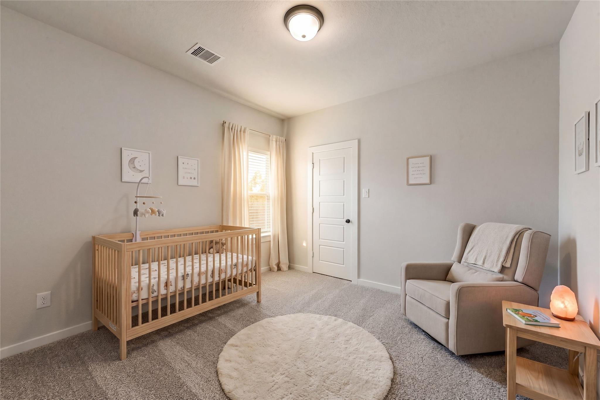 Cozy nursery featuring wooden crib with mobile, beige rocking chair, fluffy rug in Davidson Homes Everett C, Sundance Cove, Crosby Texas
