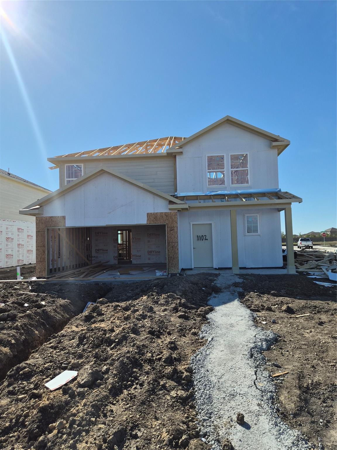Two-story 4-bedroom home under construction with beige siding, red roof, and open garage framing in Emberly, Beasley, Texas by Davidson Homes The Tierra B