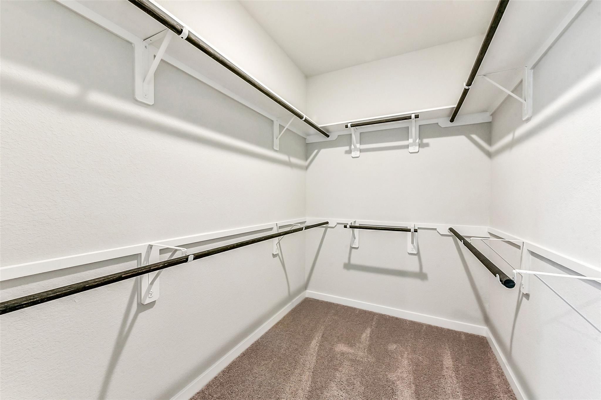 Spacious walk-in closet with built-in wooden shelving and metal hanging rods in Davidson Homes The Costa B, Dayton, Texas