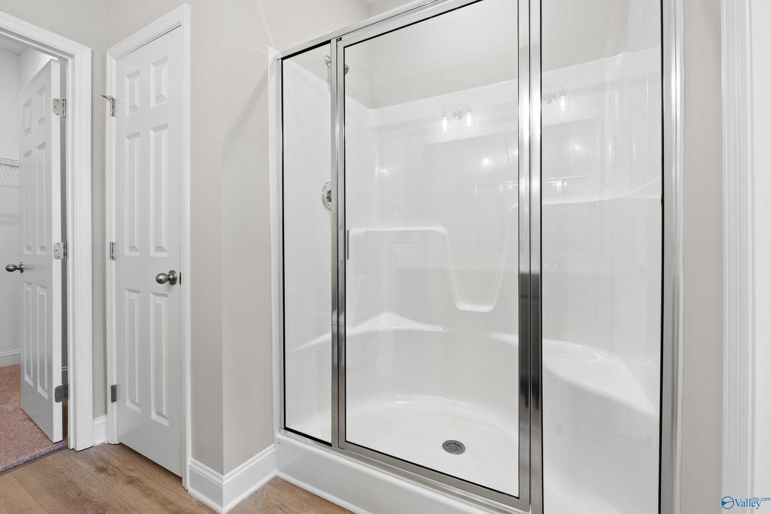 Modern master bathroom with frameless glass shower, white tile, and adjacent doors in Davidson Homes The Asheville C, Athens, AL