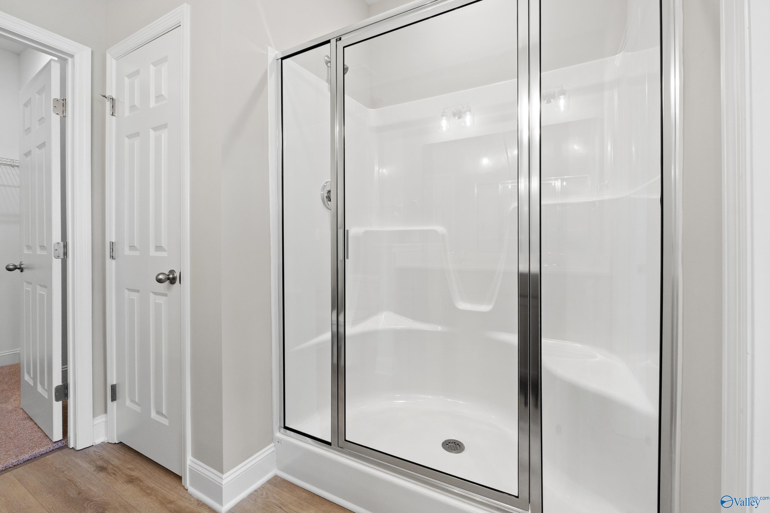 Modern master bathroom with frameless glass shower, white tile, and adjacent doors in Davidson Homes The Asheville C, Athens, AL