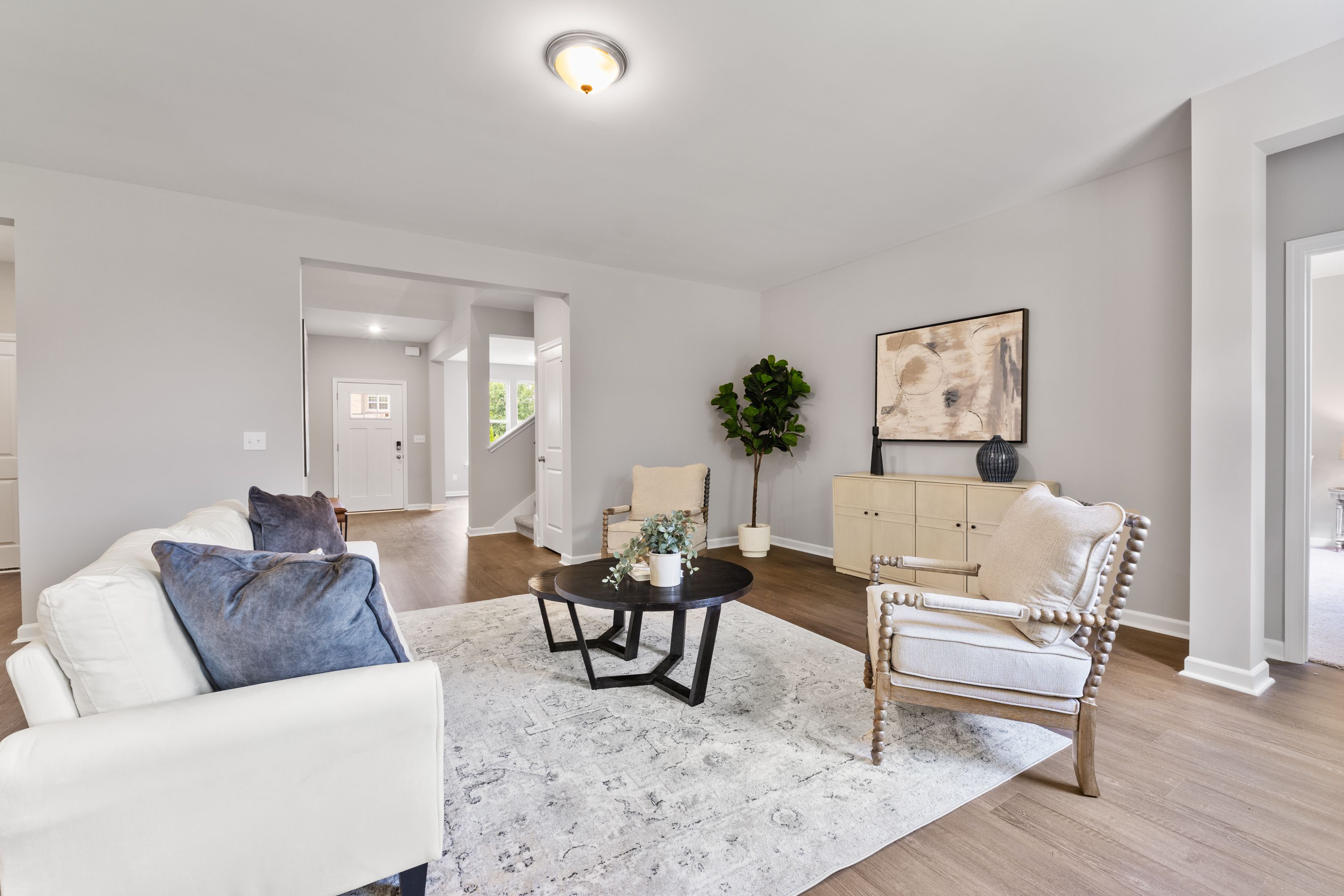Spacious living room in The Avalon E with white sofa, beige armchair, black coffee table, potted plants, and open archways