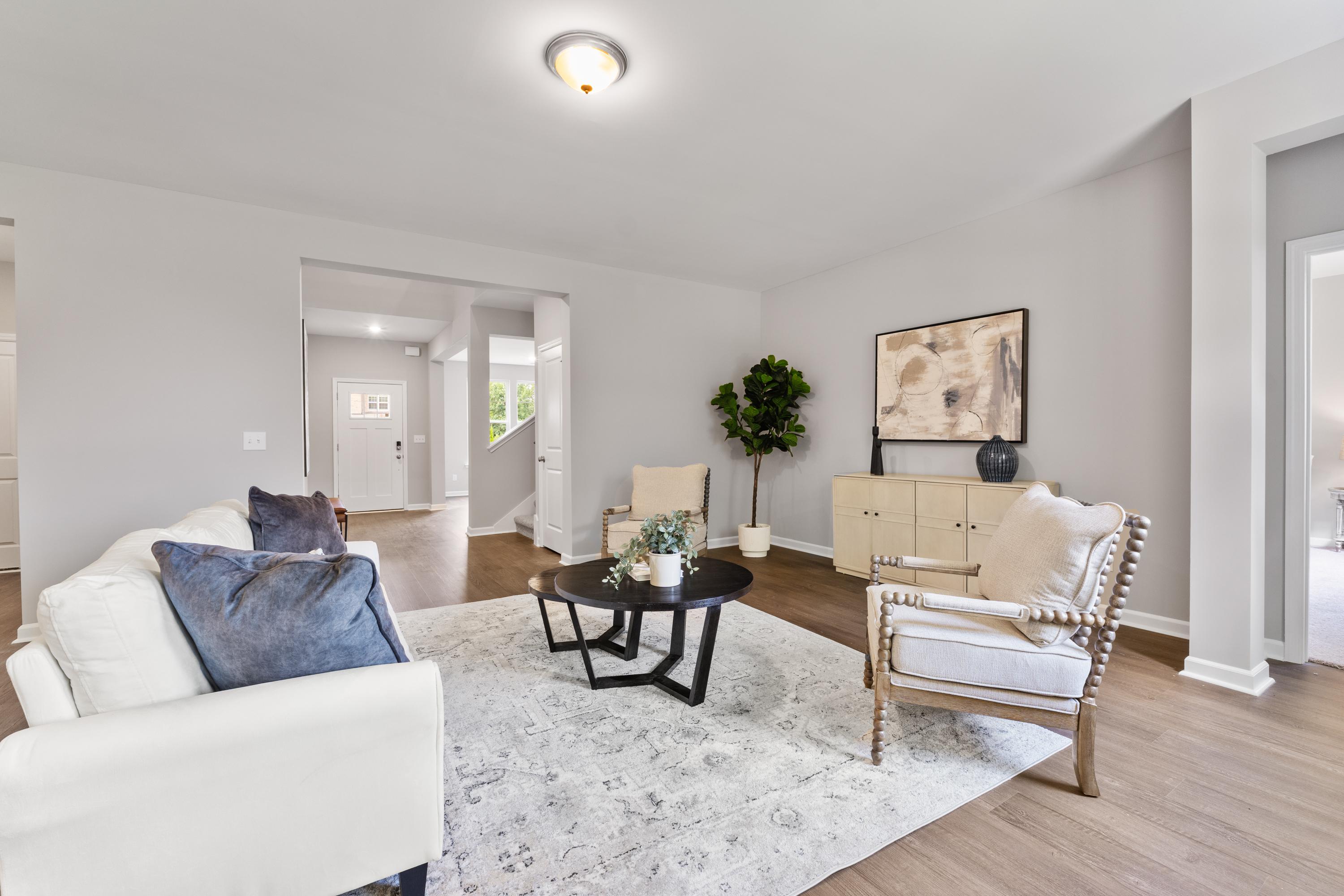 Spacious living room in The Avalon D home with white sofa, beige armchair, wooden coffee table, potted plants, and open layout