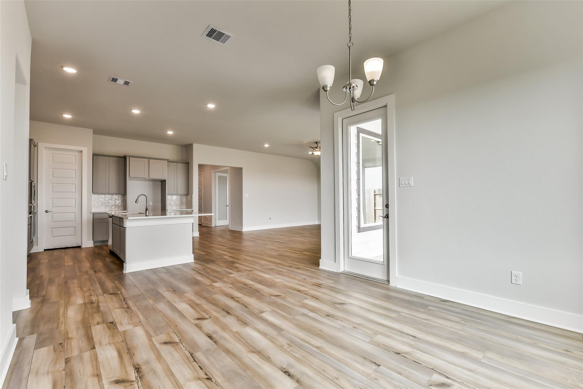 Open-concept kitchen with white cabinets, large island, and hardwood floors opening to living area with French doors in Davidson Homes The George A, Lago Mar