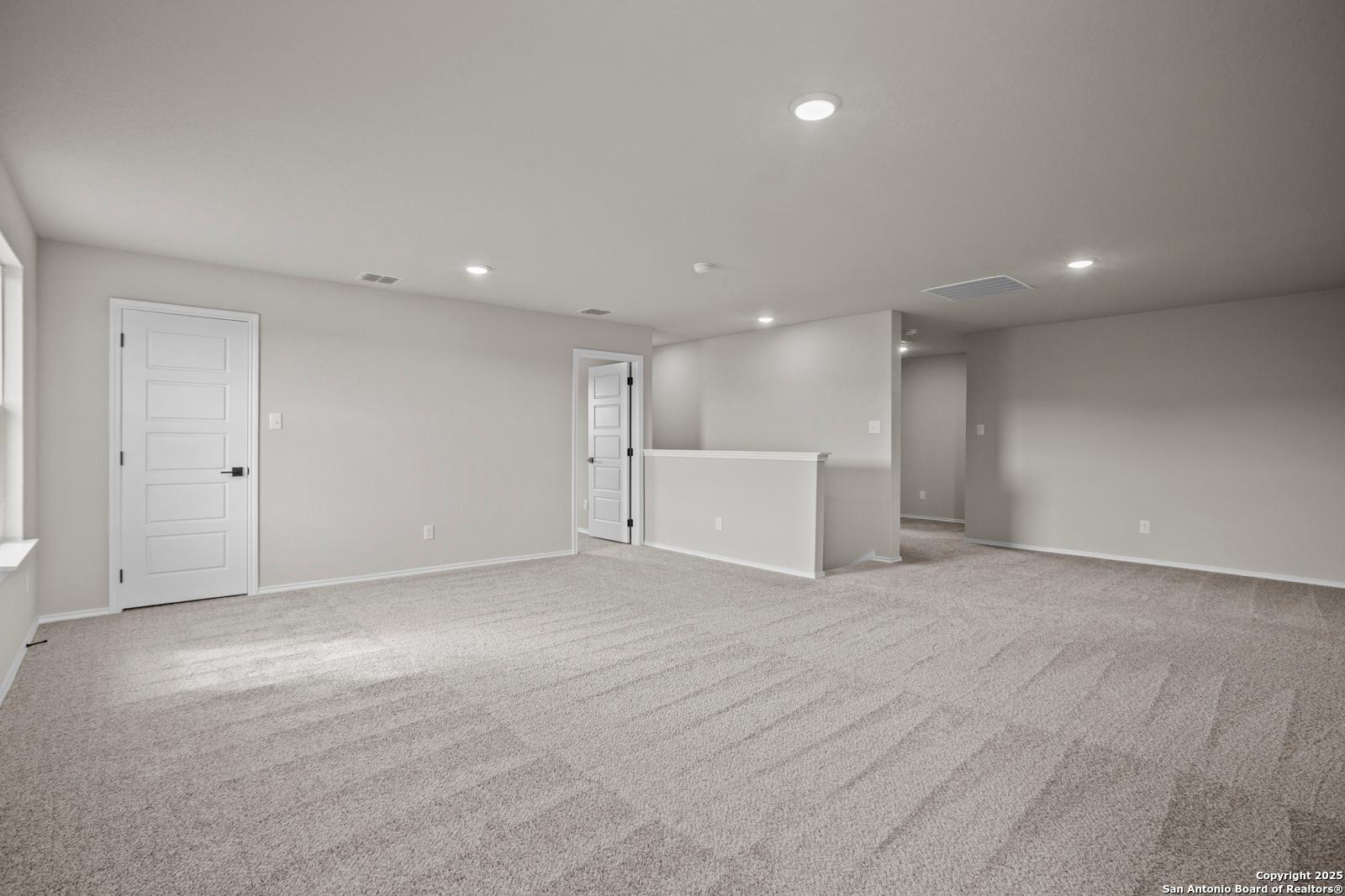 Spacious upstairs bonus room with beige carpet, white doors, and overlooking railing in Davidson Homes The Douglas F, San Antonio