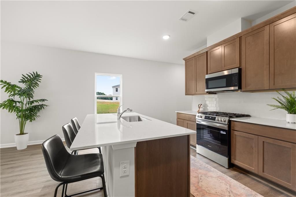 Modern kitchen with white quartz island, wood cabinets, and stainless steel appliances in The Sinclair B, Cedar Farms.