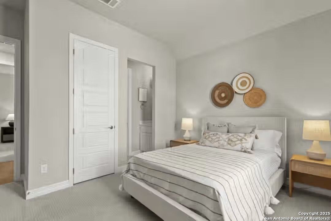 Cozy bedroom with light gray walls, striped bedding, woven wall art, and en-suite door in Davidson Homes The Summerlin B, Castroville, Texas